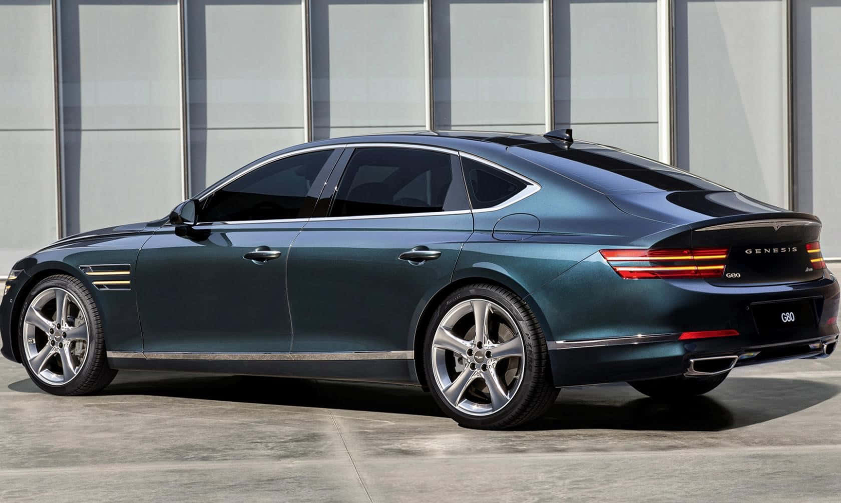 Genesis G80 桌布 壁紙 — 一輛時尚深青綠色Genesis G90豪華轎車停在混凝土上，以現代玻璃建築為背景。