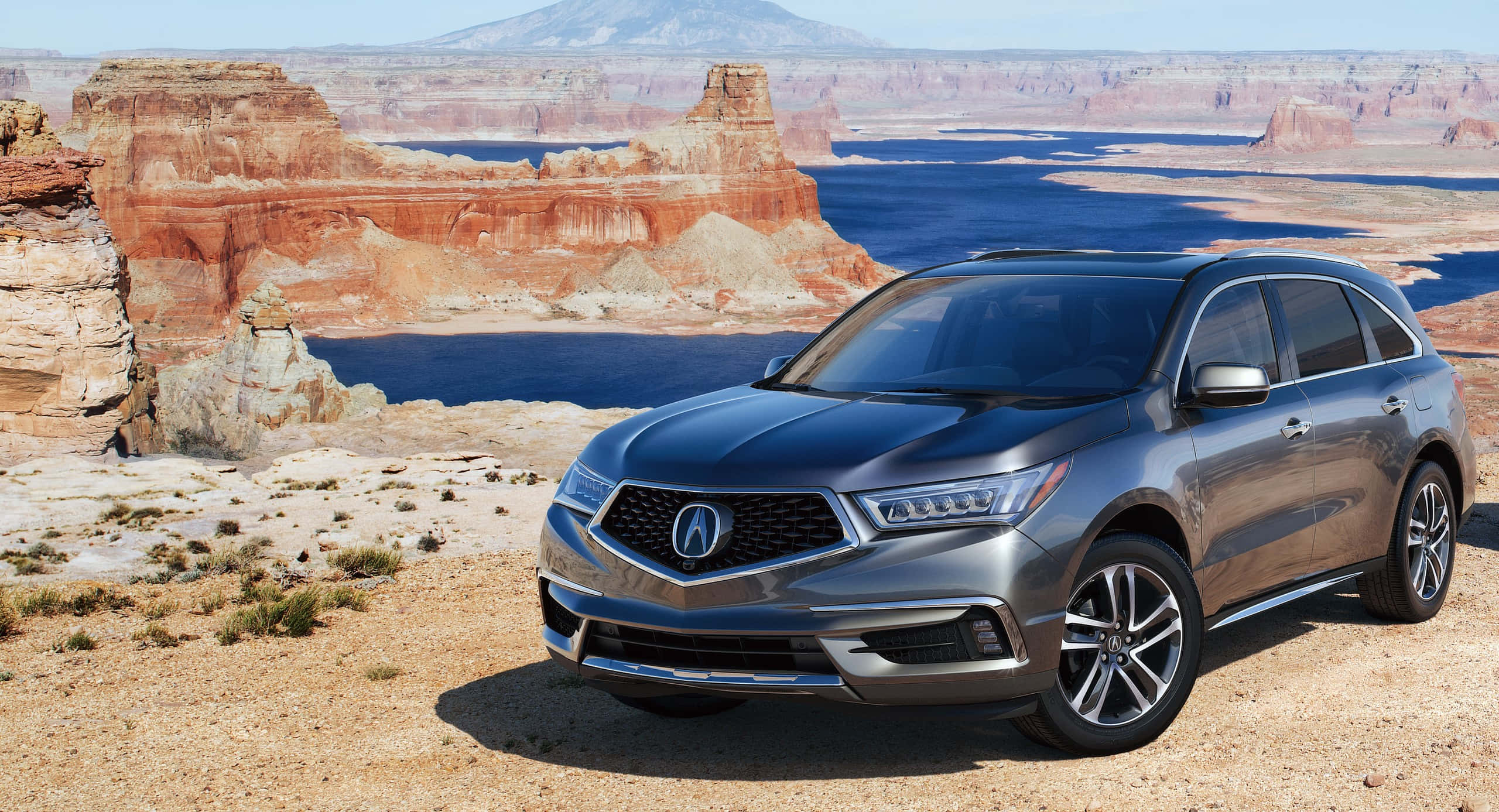 Acura Mdx 桌布 壁紙 — 一輛時尚灰色Acura SUV停泊在沙漠地形上，背景有紅色岩石形成和藍色湖泊，天空晴朗。