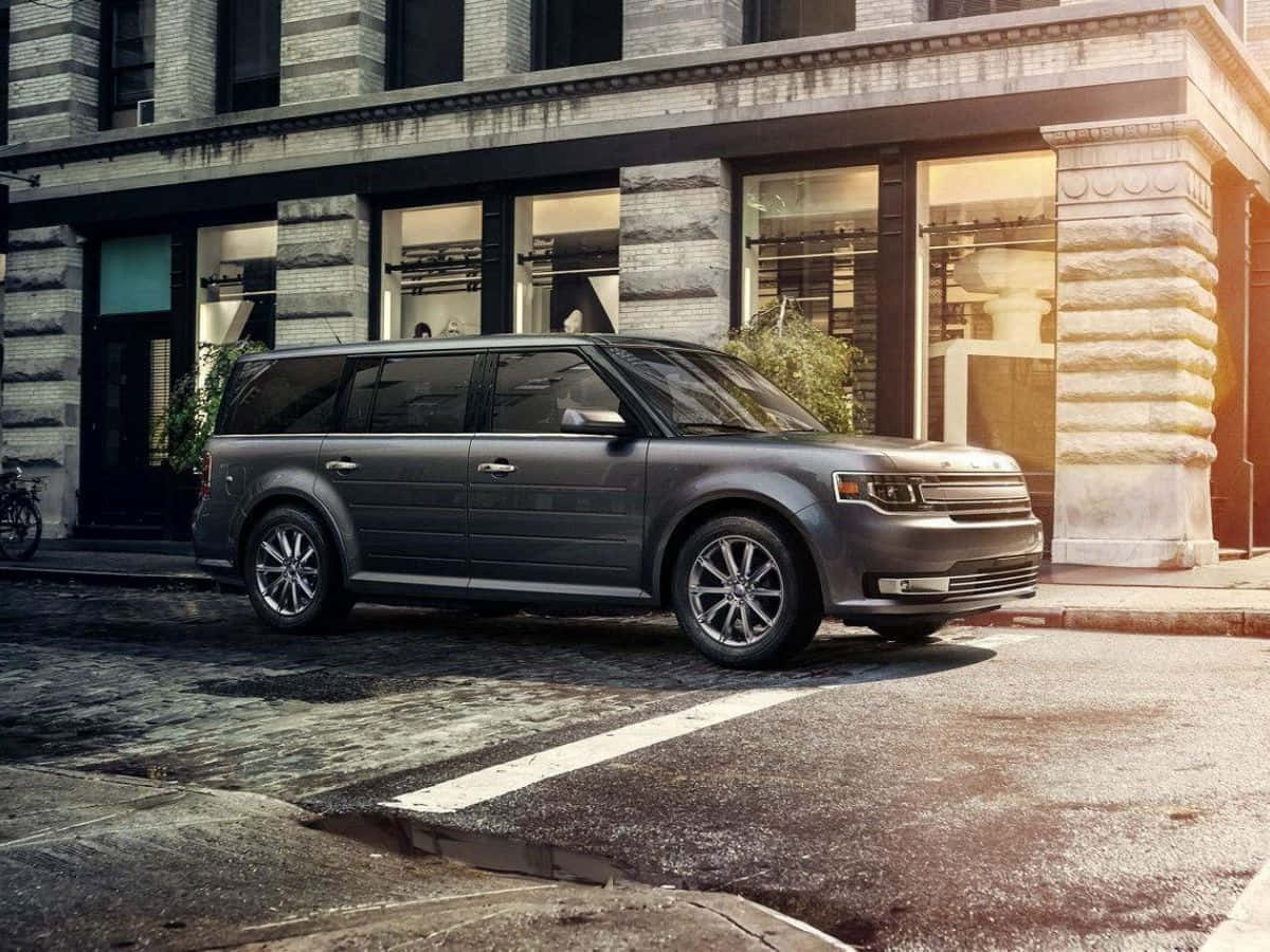 Ford Flex 桌布 壁紙 — 一輛時尚灰色SUV停泊在鵝卵石街道上，旁邊是一棟有大窗戶的歷史石建築。