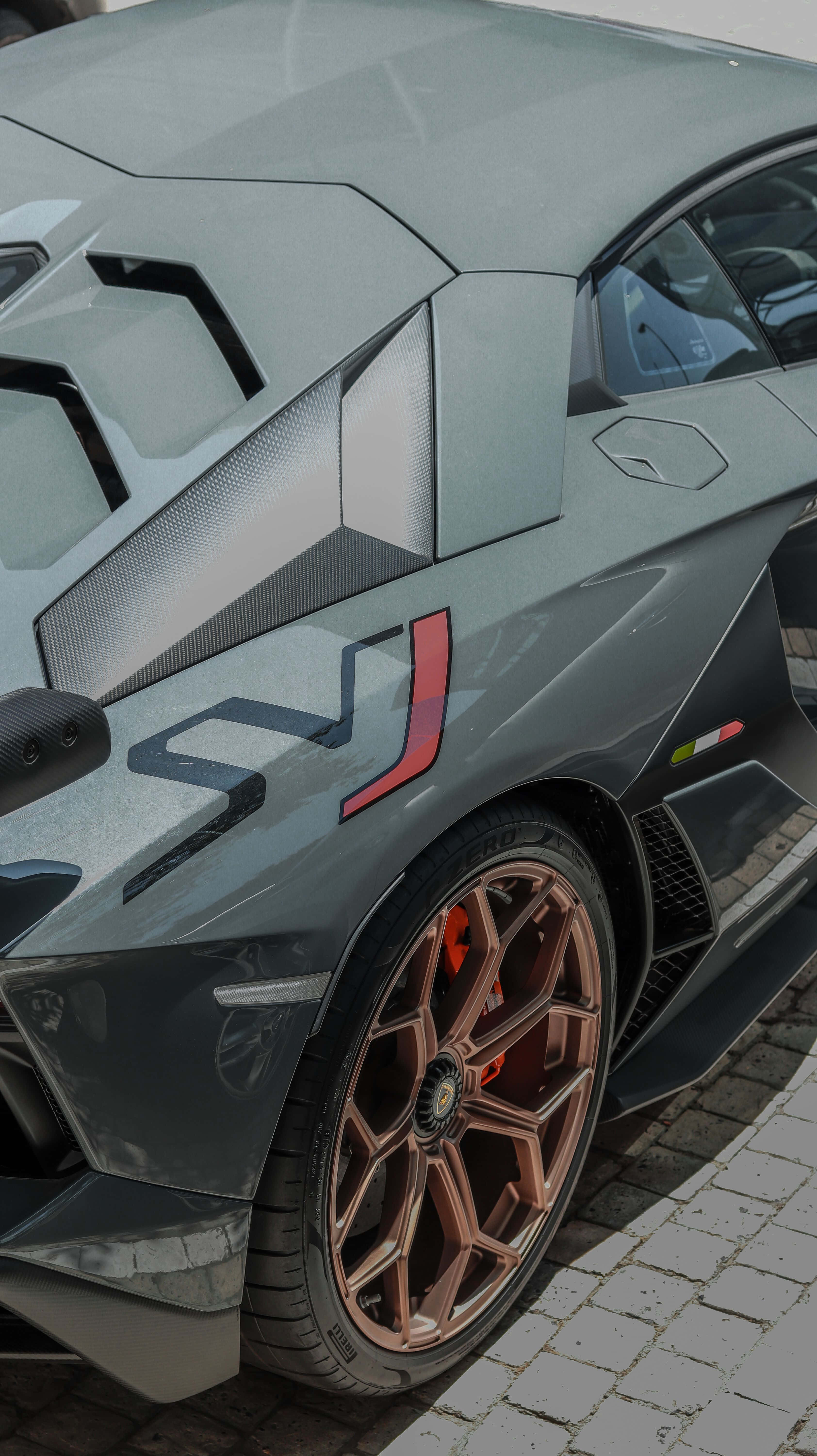 race car 桌布 壁紙 — 一輛時尚灰色藍寶堅尼配青銅輪圈及紅色制動卡鉗，停泊在鵝卵石路上的特寫。