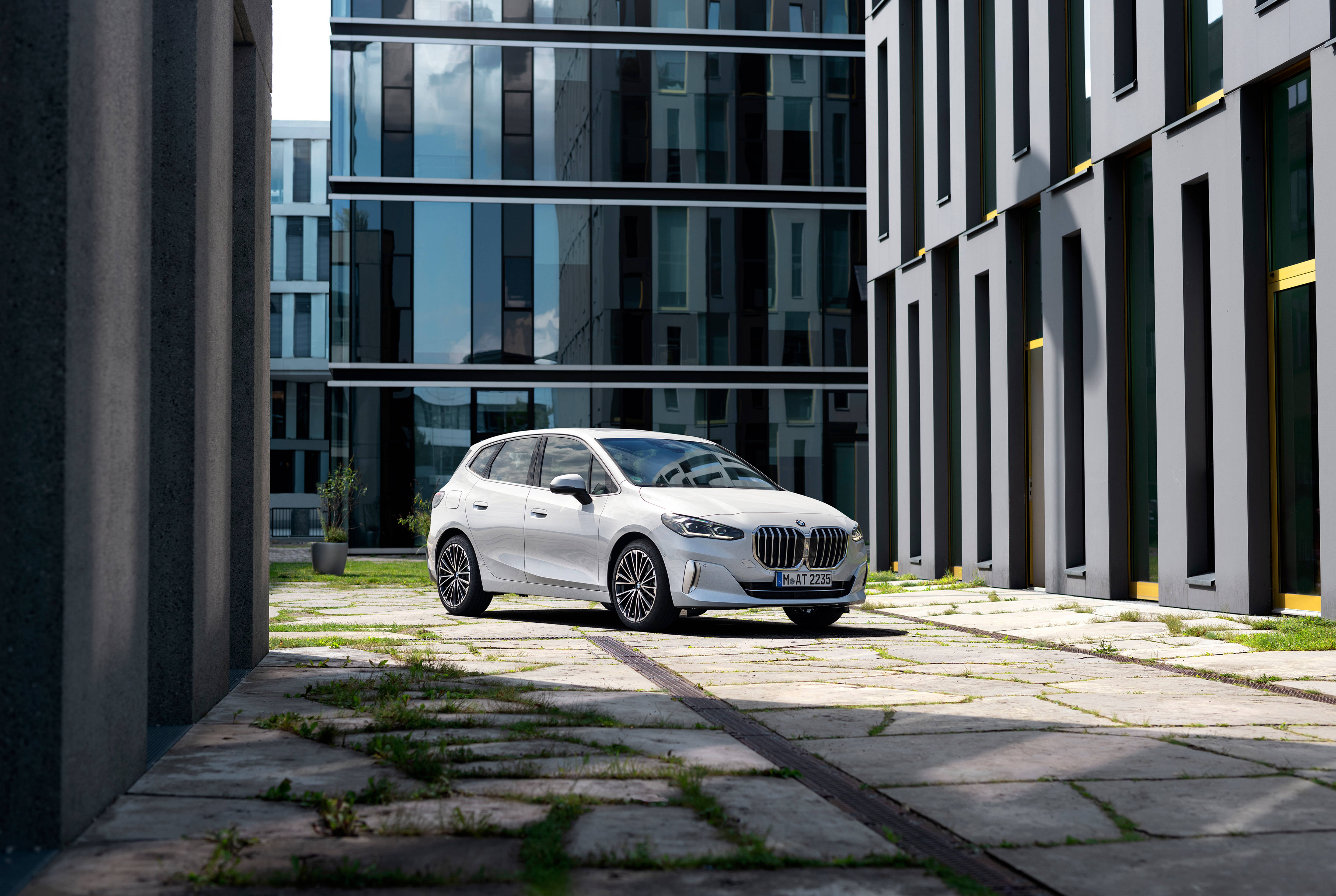 Luxury 桌布 壁紙 — 一輛時尚白色BMW掀背車停放在現代玻璃與灰色混凝土建築之間，石鋪地上長出青草。