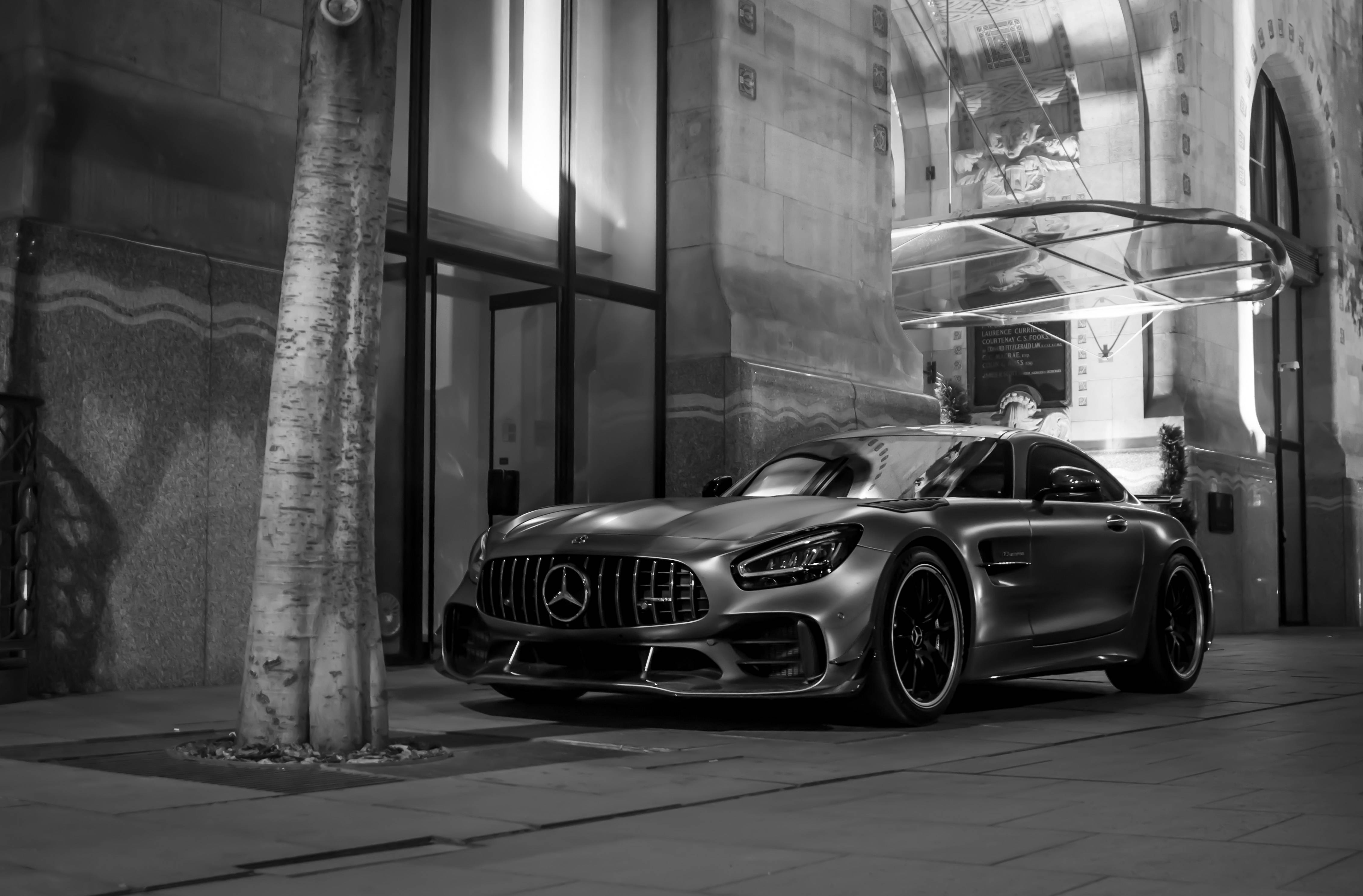 R 桌布 壁紙 — 一輛時尚的 Mercedes-AMG GT 在夜間停在一棵樹旁，前面是一座宏偉的建築，燈光效果戲劇化。