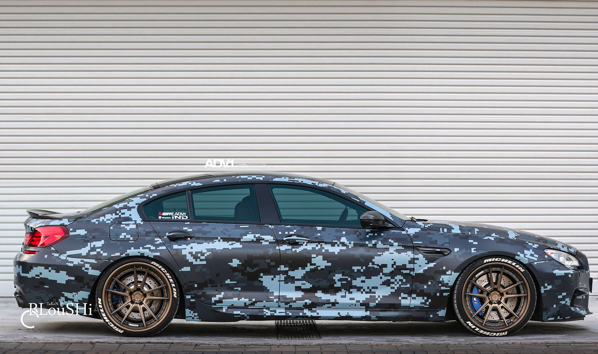 m 桌布 壁紙 — 一輛時尚的BMW M5跑車，帶有數位迷彩包膜，停靠在波紋金屬車庫門前。
