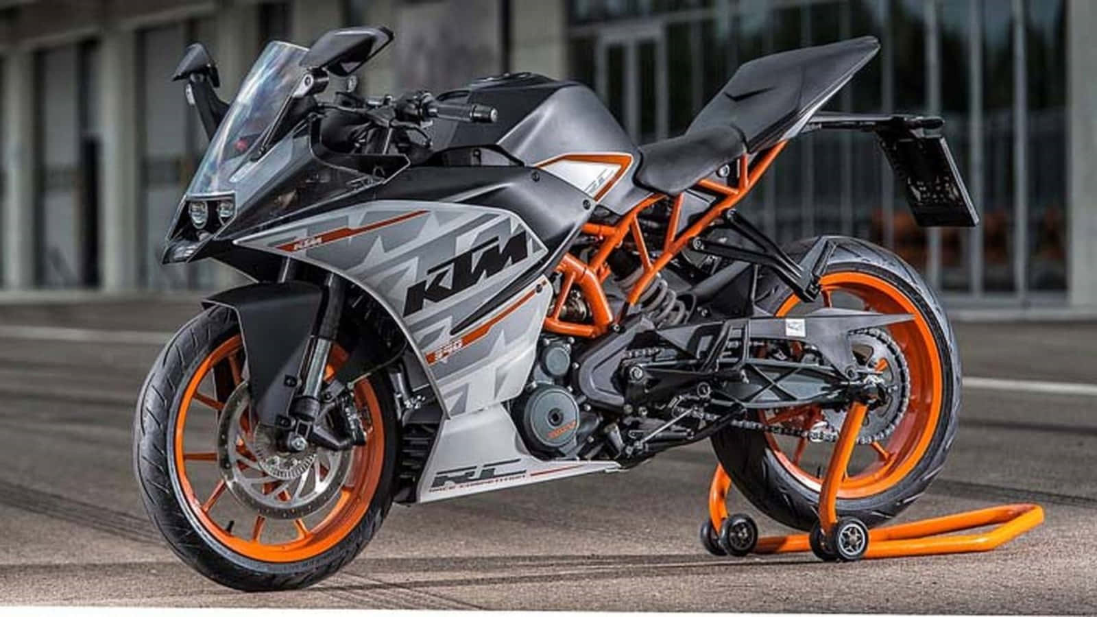  壁紙 — 一輛時尚的KTM RC 390機車，帶有橙色和灰色點綴，停在鋪砌路面上的亮橙色支架上。