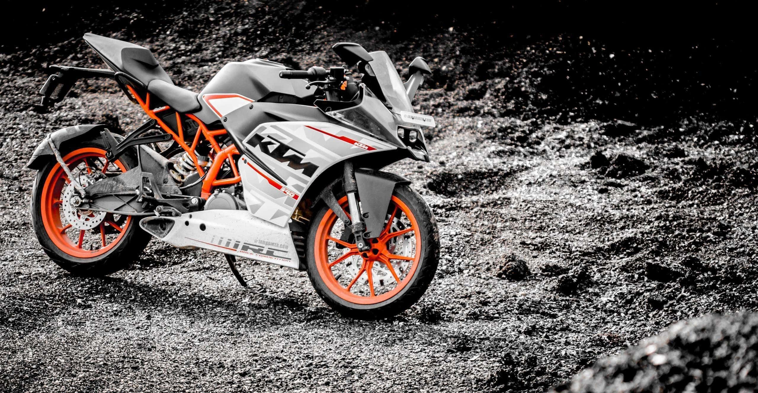 Ktm Bike 桌布 壁紙 — 一輛時尚的KTM機車，配以鮮豔的橙色輪框，在強烈黑白對比燈光下，立於碎石地面上。