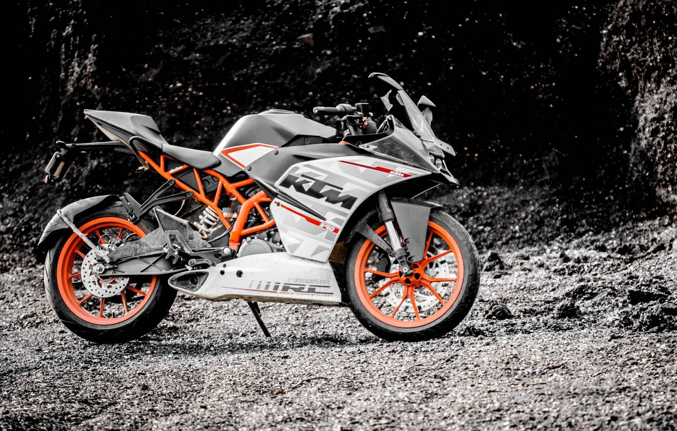 motorbike 桌布 壁紙 — 一輛時尚的KTM運動機車帶有鮮豔的橙色點綴，立於粗糙的礫石表面上，背景為深色紋理。