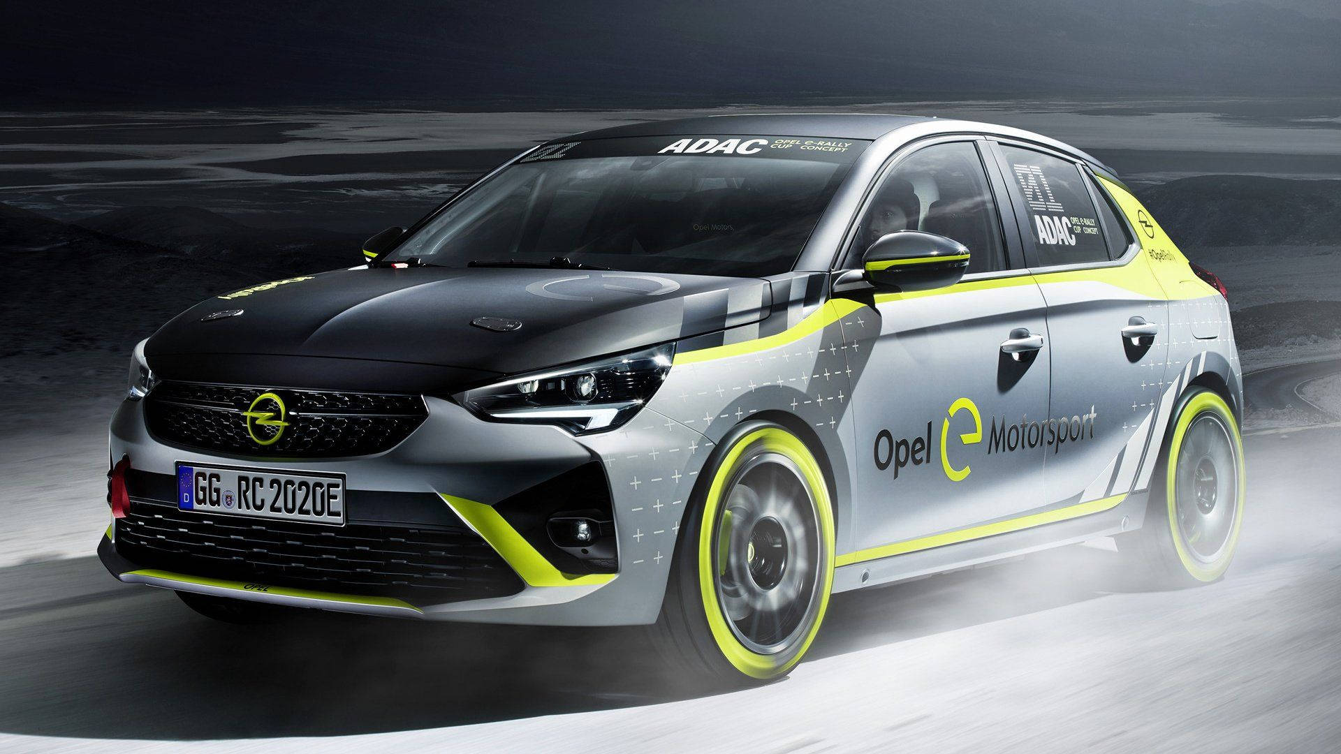 Opel 桌布 壁紙 — 一輛時尚的Opel e-Motorsport賽車帶有鮮豔的黃色點綴，在戲劇性的夜間燈光下在霧濛濛的瀝青賽道上疾馳。