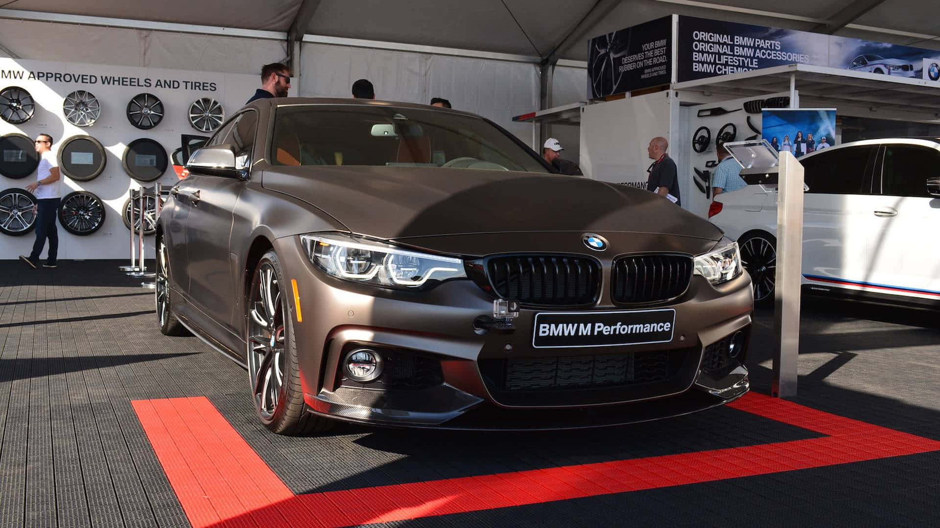 Bmw 440i 桌布 壁紙 — 一輛時尚的啞光棕色BMW M4雙門轎跑車在車展帳篷內展出，配有紅地毯和輪胎展品。