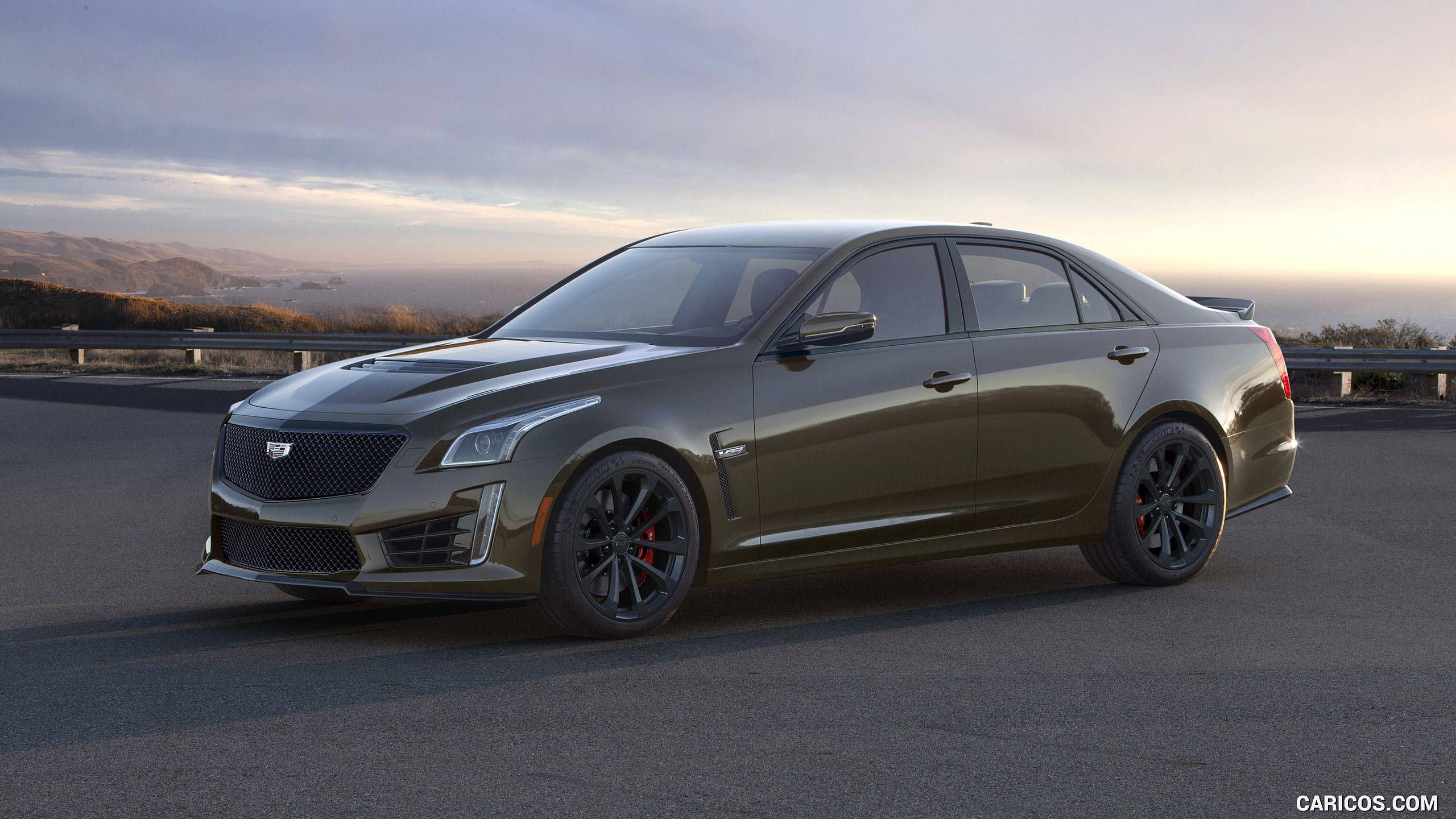 Cadillac 桌布 壁紙 — 一輛時尚的啞光橄欖綠色凱迪拉克CTS-V轎車，配備黑色輪圈和紅色制動卡鉗，停在日落時分的沿海公路上。