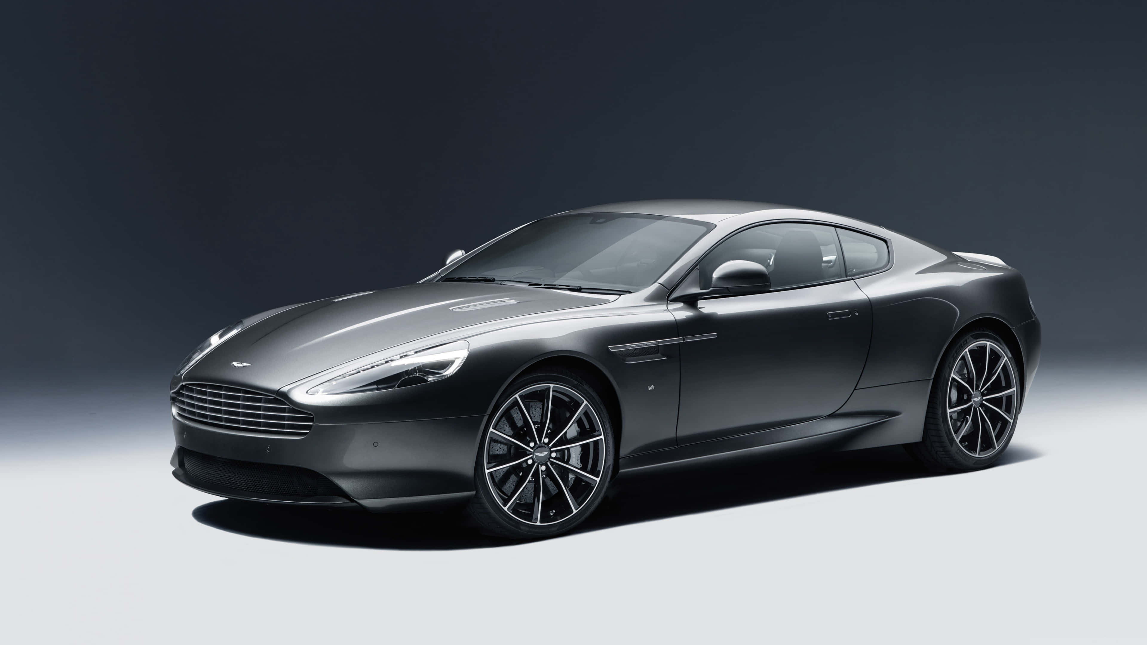奧斯頓馬丁 桌布 壁紙 — 一輛時尚的啞光灰色 Aston Martin 跑車在攝影棚燈光下，在深色漸變背景上閃耀。