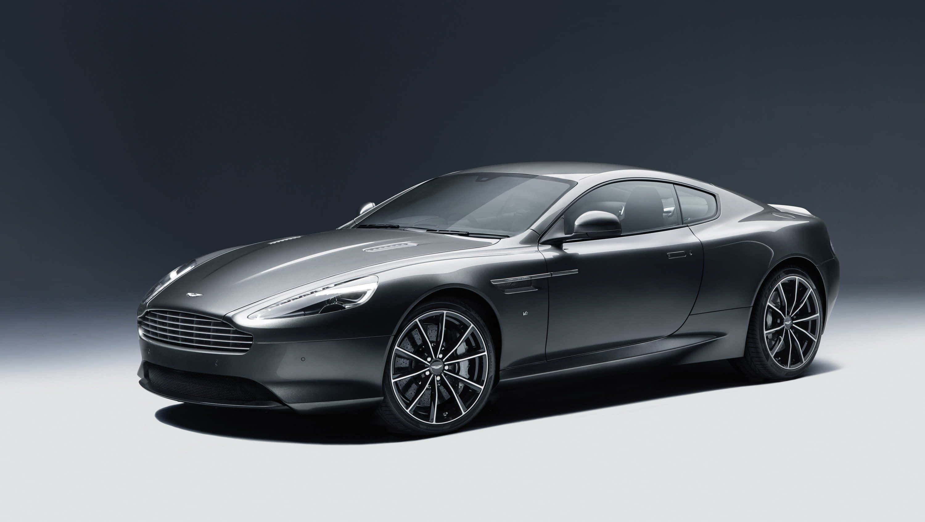 Aston Martin Db9 桌布 壁紙 — 一輛時尚的啞光灰色 Aston Martin 跑車在攝影棚燈光下，於灰色漸變背景前滑行。