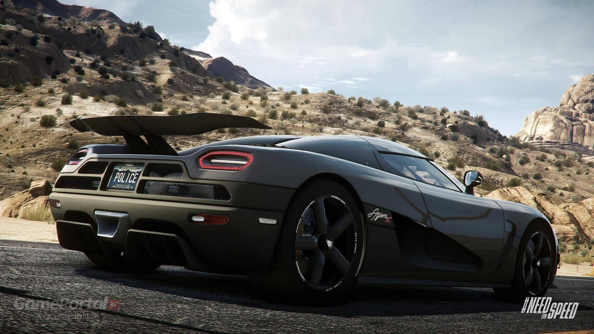 Need For Speed 桌布 壁紙 — 一輛時尚的啞光灰色 Koenigsegg Agera R 警車，展開後翼，在晴朗天空下沿著沙漠公路疾馳，兩旁是岩石丘陵。