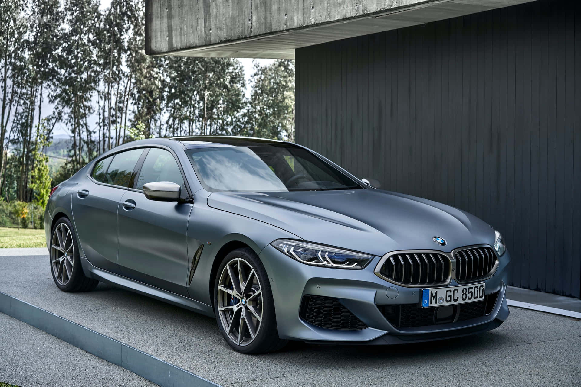 Bmw 8 Series 桌布 壁紙 — 一輛時尚的啞光灰色BMW 8系列轎跑車停在現代混凝土懸挑下，背景有樹木。