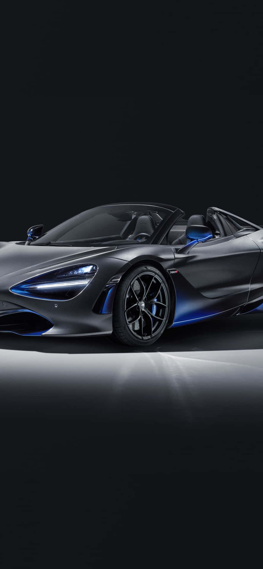  壁紙 — 一輛時尚的啞光灰色McLaren 720S Spider，帶有發光的藍色飾邊和頭燈，在黑暗的攝影棚背景下照亮。