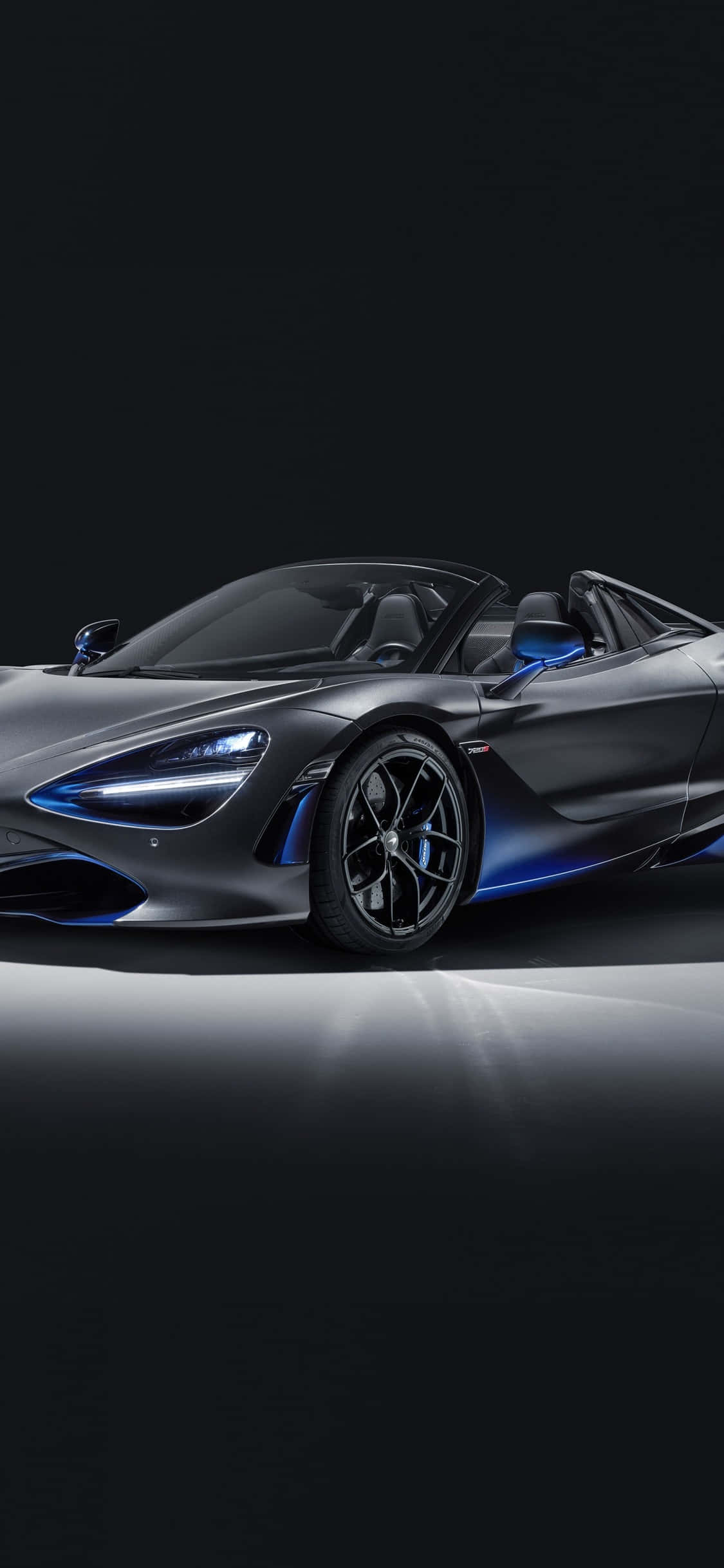 Black Car 桌布 壁紙 — 一輛時尚的啞光灰色McLaren 720S Spider，帶有發光的藍色點綴，停放在黑色背景的反射表面上。