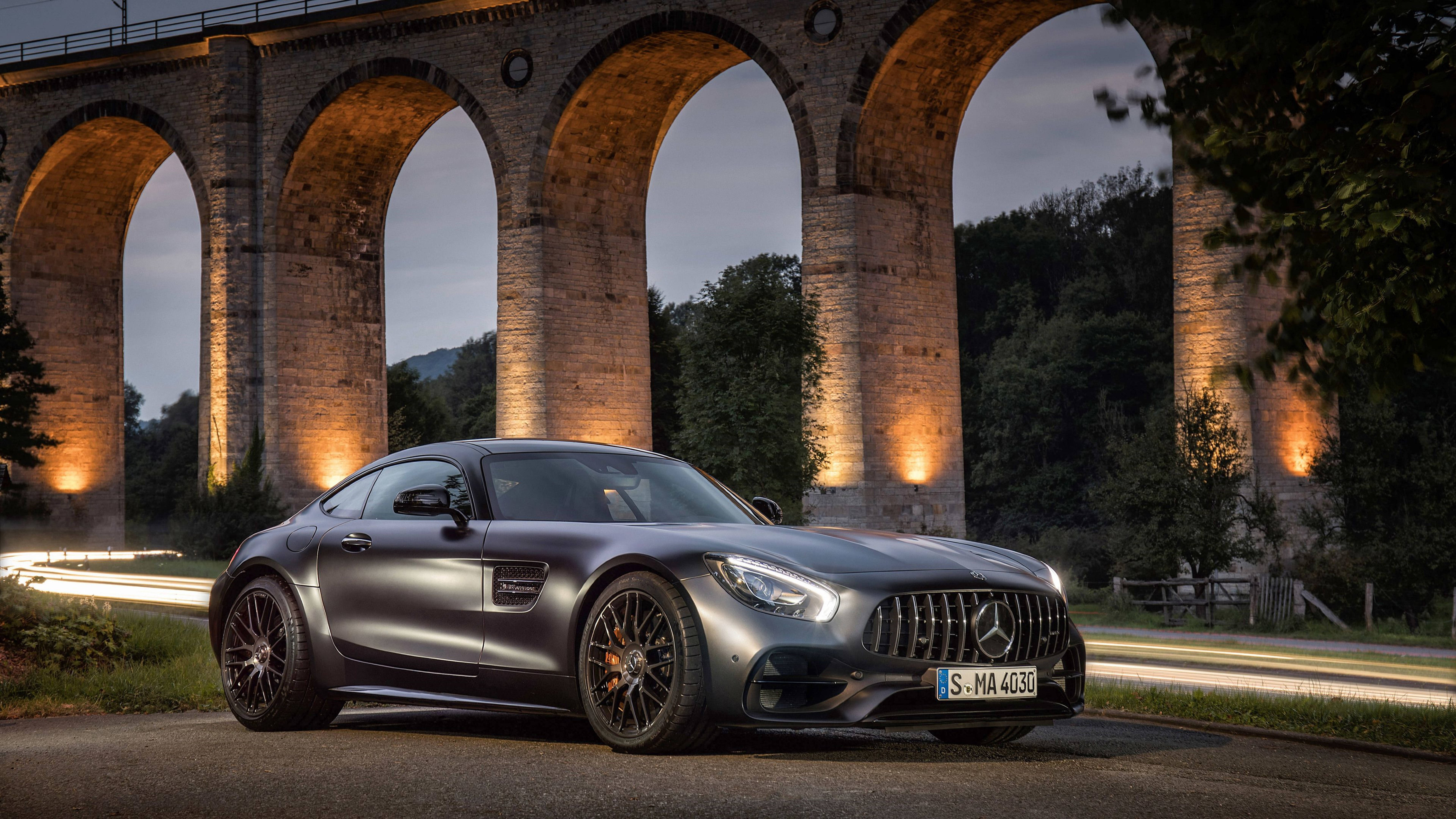 Mercedes 桌布 壁紙 — 一輛時尚的啞光灰色Mercedes-AMG GT在黃昏時停泊在溫暖照明的石拱橋下。