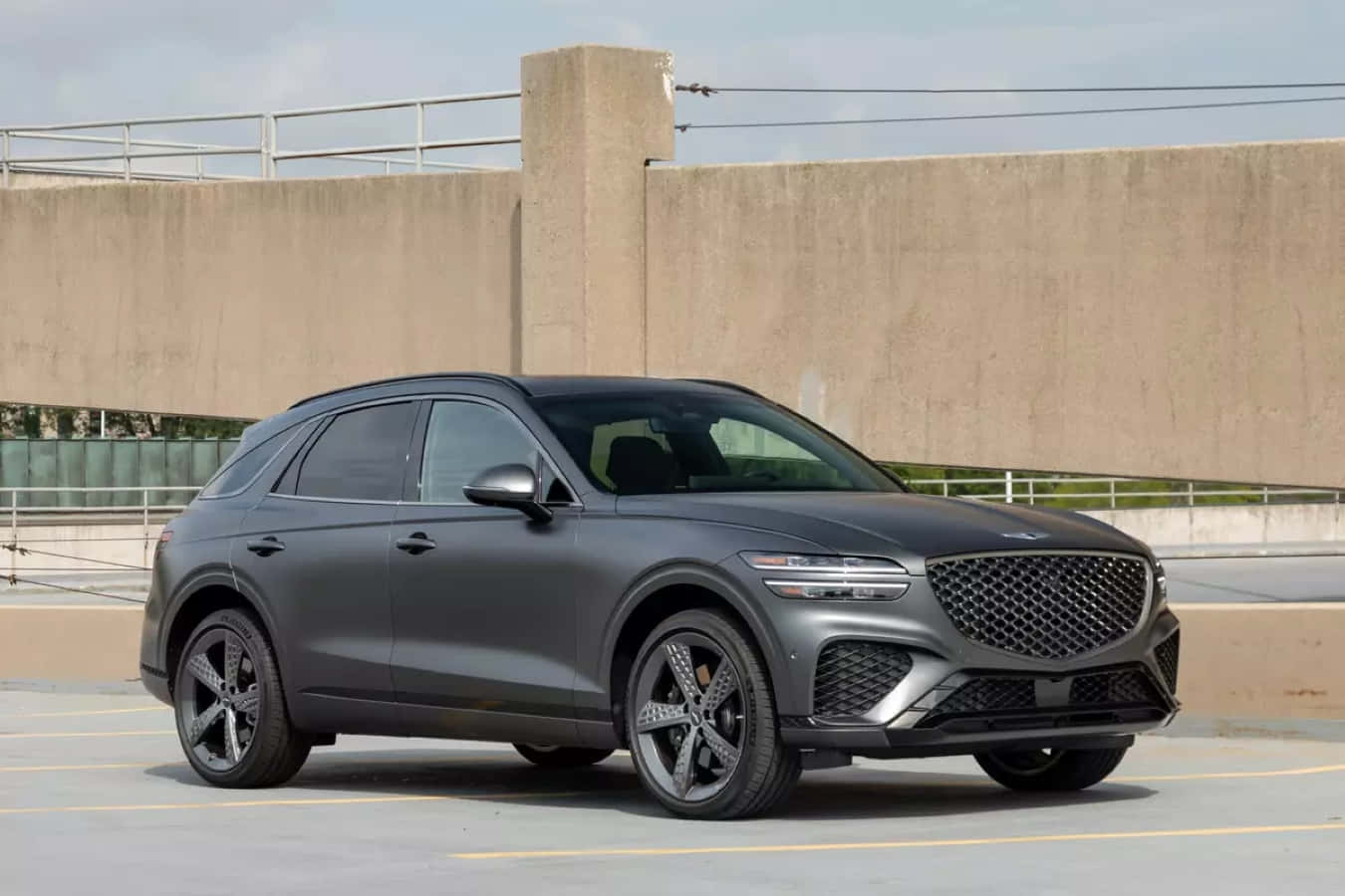 Genesis Gv70 桌布 壁紙 — 一輛時尚的啞光灰色SUV停放在混凝土停車場，周圍是工業風格的牆壁和欄杆，在明亮的日光下。