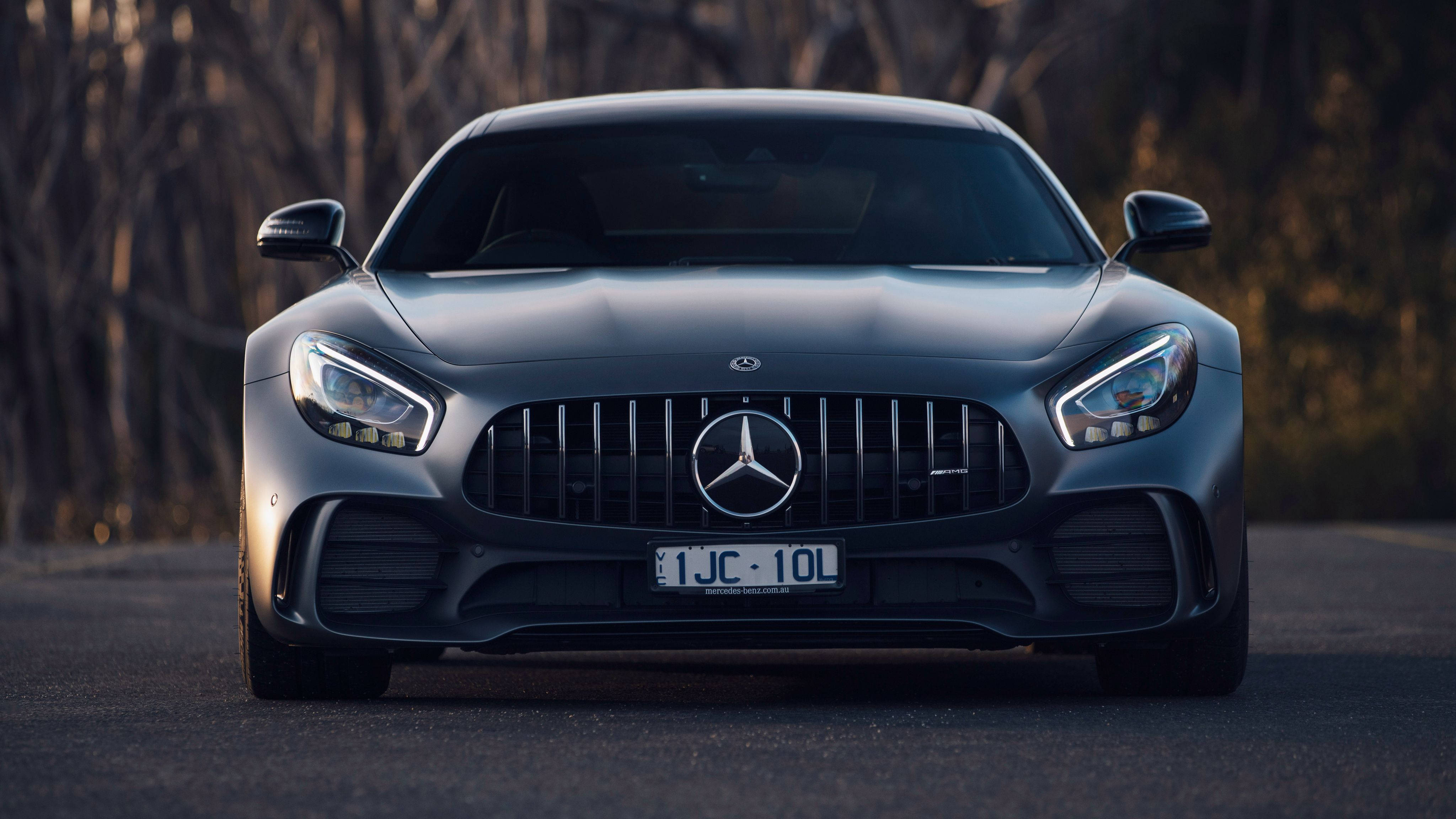 4K 奔馳壁紙 桌布 壁紙 — 一輛時尚的啞光灰色梅賽德斯-AMG GT跑車在道路上向前行駛，背景有模糊的樹木。