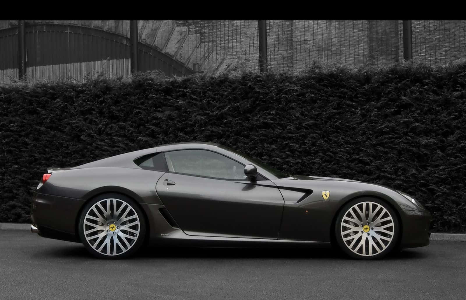 Ferrari 599 Gtb Fiorano 桌布 壁紙 — 一輛時尚的啞光灰色法拉利跑車停靠在茂密樹籬旁，在柔和日光下。
