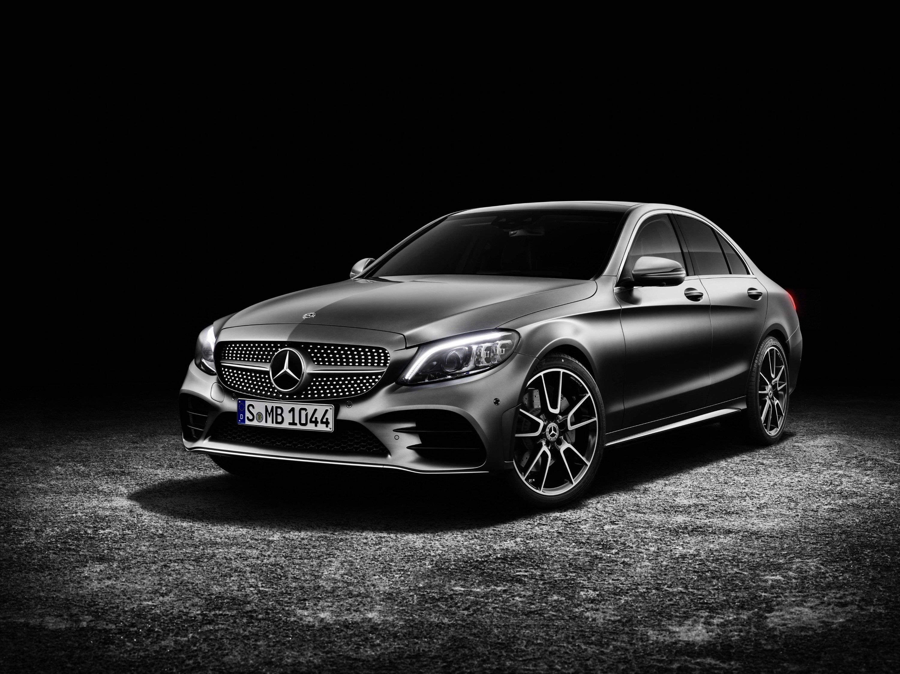 Mercedes Benz C300 桌布 壁紙 — 一輛時尚的啞光灰色賓士C-Class轎車在黑色背景上，於紋理瀝青表面上戲劇性地被照亮。