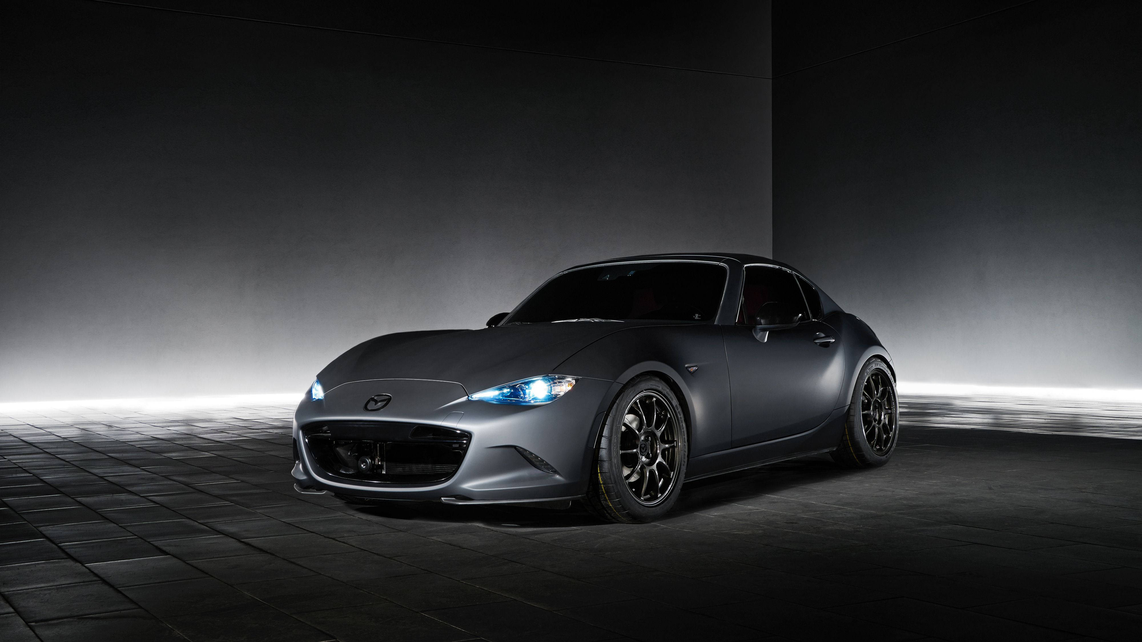 Mazda 桌布 壁紙 — 一輛時尚的啞光灰色跑車，帶有發光的藍色車頭燈，在黑暗的攝影棚中，有霧氣和瓷磚地板，戲劇性地照亮。