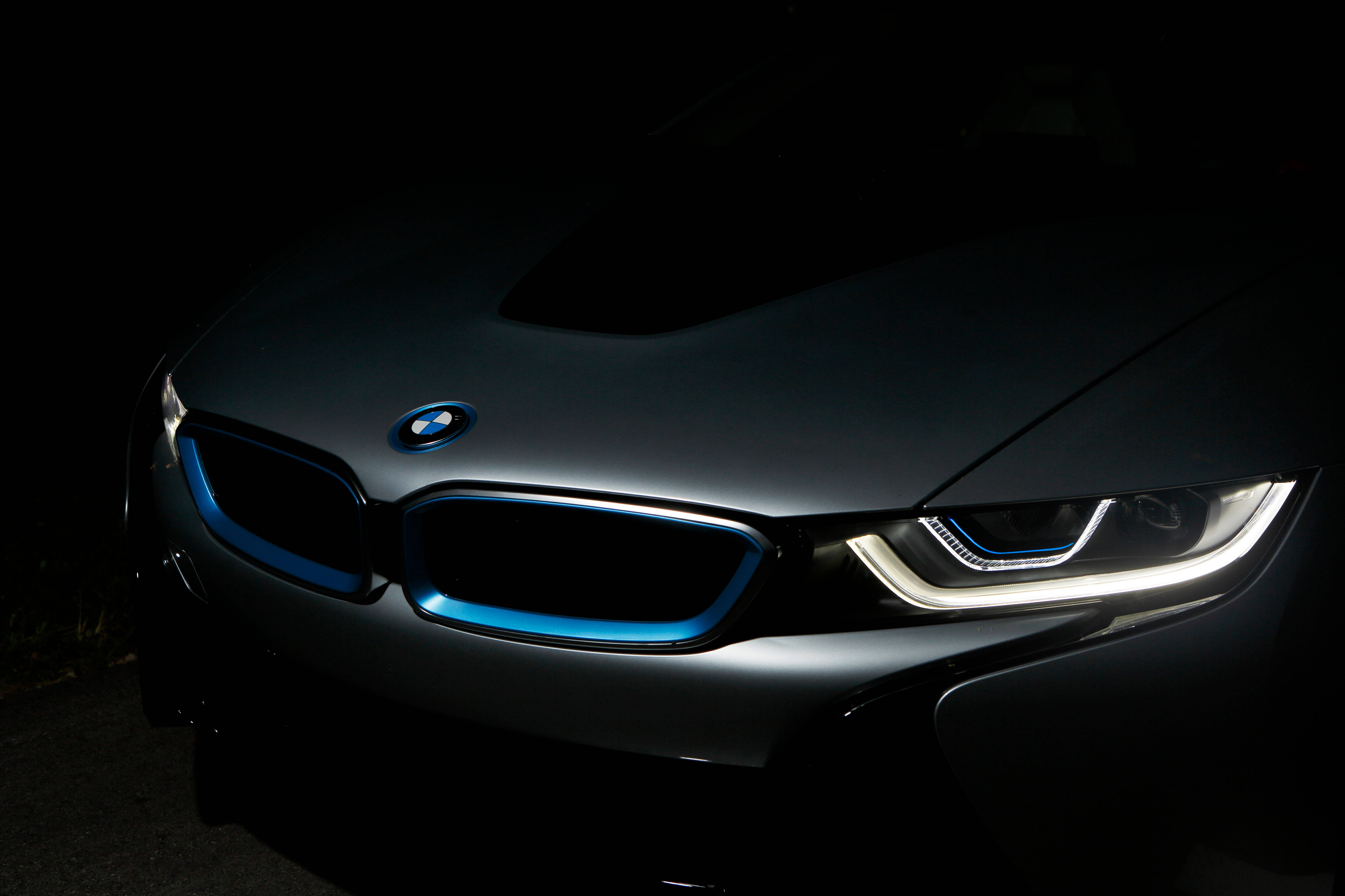 BMW 動圖 桌布 壁紙 — 一輛時尚的啞光黑色BMW i8，在漆黑的夜晚背景下，被發光的藍色飾條和銳利的白色頭燈照亮。