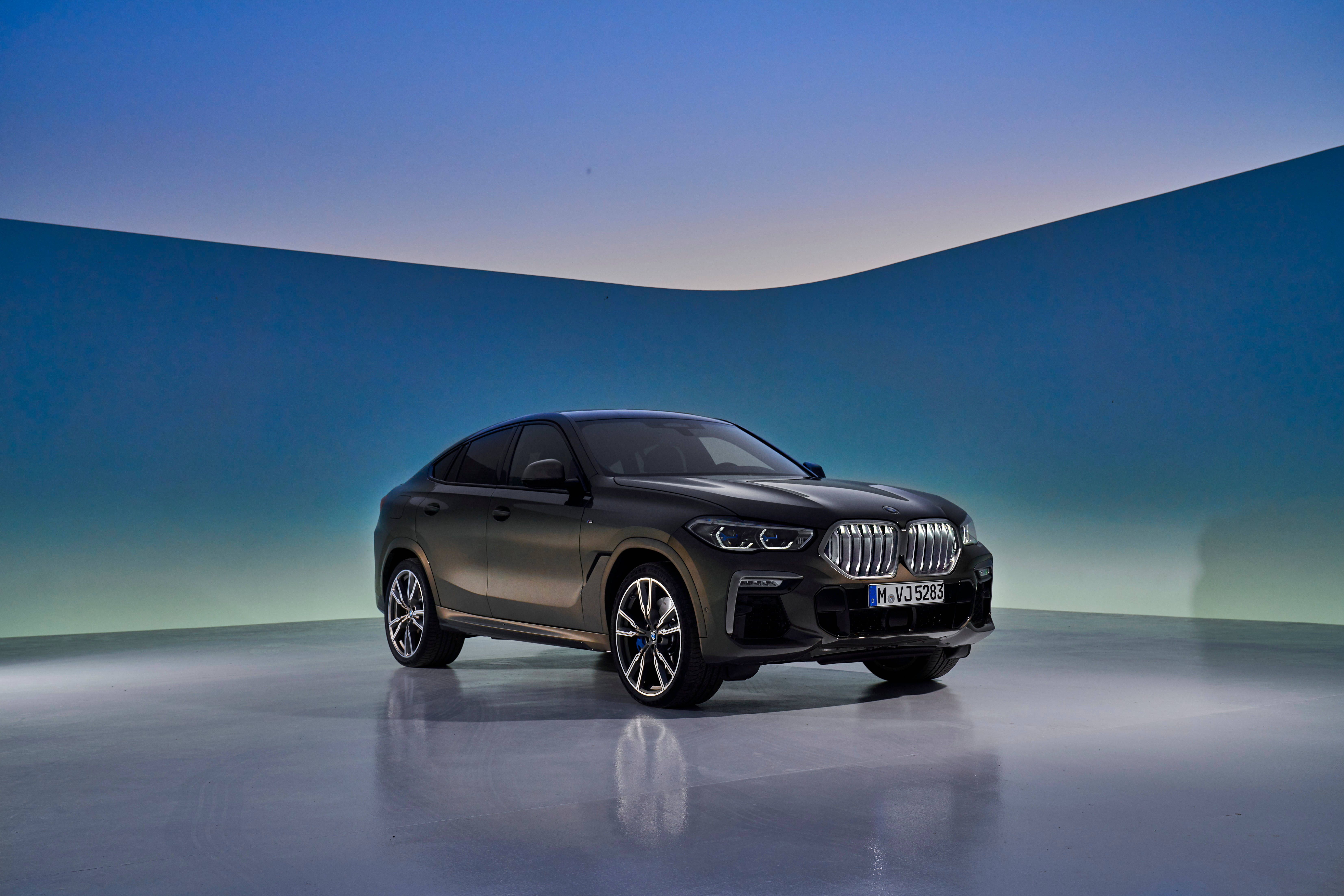m 桌布 壁紙 — 一輛時尚的啞光黑色BMW X6 SUV在攝影棚燈光下，以漸變藍綠色弧形背景為襯，閃閃發光。
