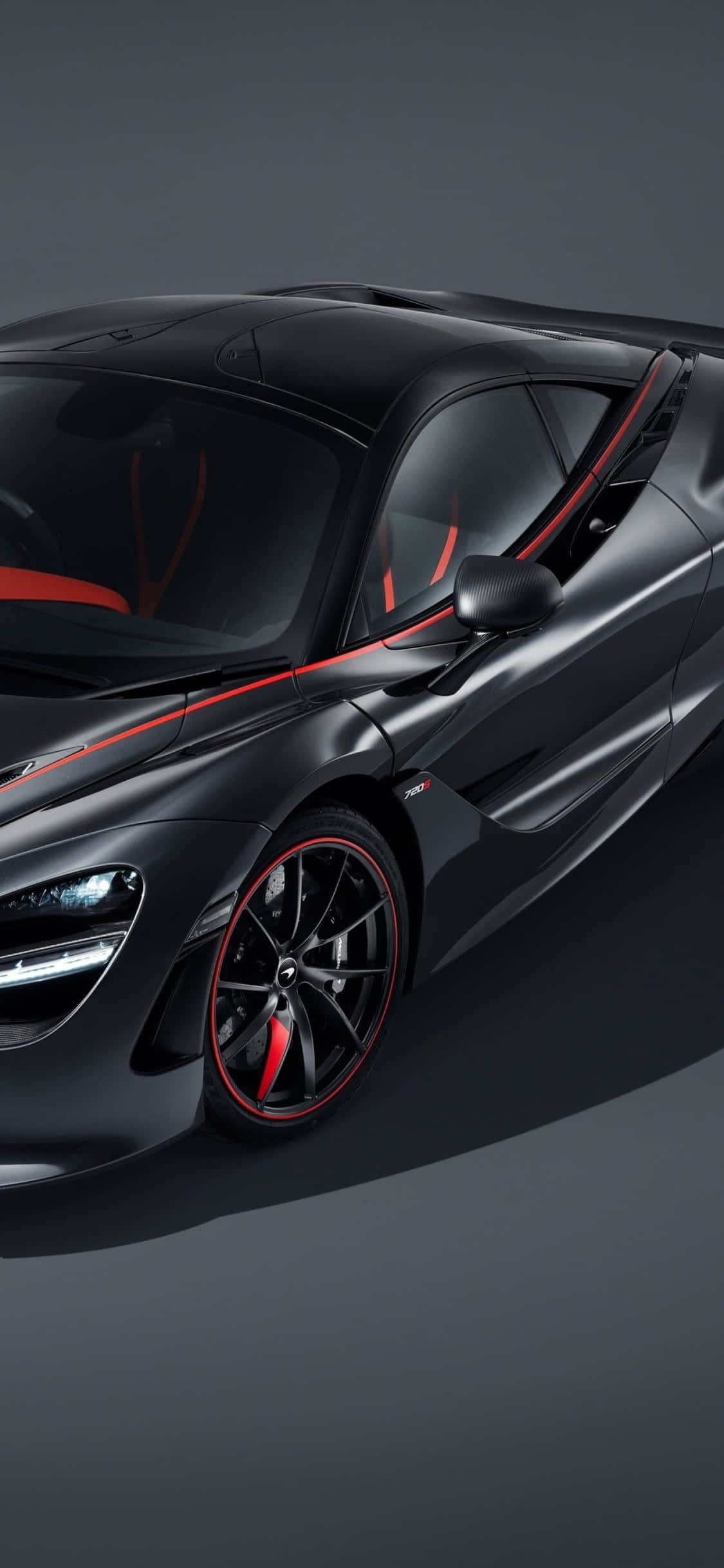 iPhone Xs Mclaren 720s 桌布 壁紙 — 一輛時尚的啞光黑色McLaren跑車，帶有紅色點綴和發光的車頭燈，以深灰色工作室背景為襯托。