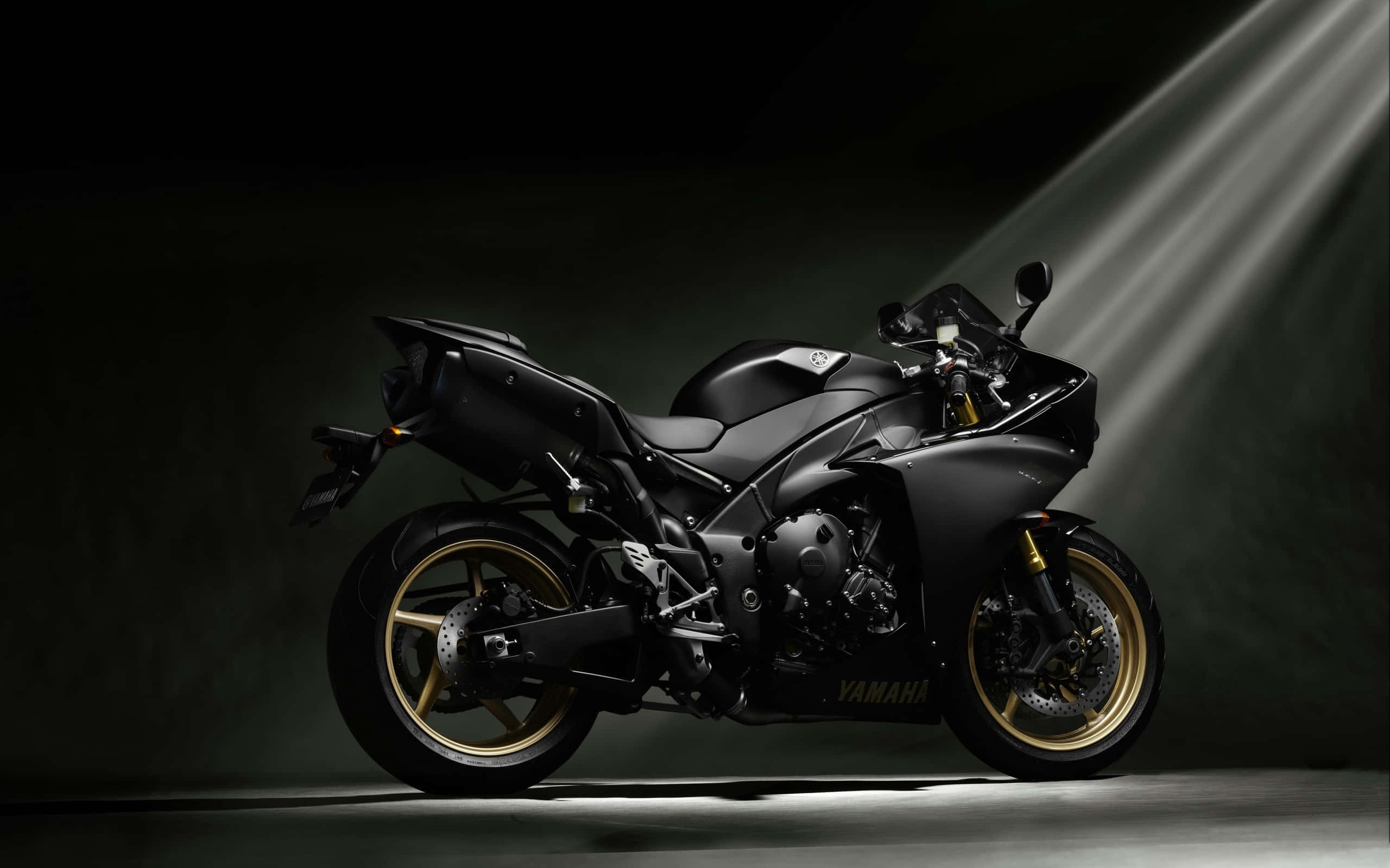 motorbike 桌布 壁紙 — 一輛時尚的啞光黑色Yamaha運動摩托車帶有金色點綴，在黑暗的攝影棚背景下被聚光燈戲劇性地照亮。
