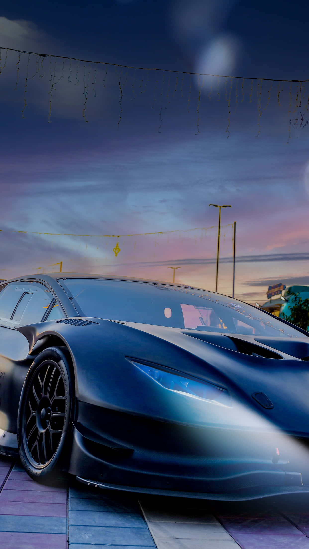 Blue Lamborghini iPhone 桌布 壁紙 — 一輛時尚的啞光黑色跑車在暮色天空下閃耀，上方懸掛著仙女燈。