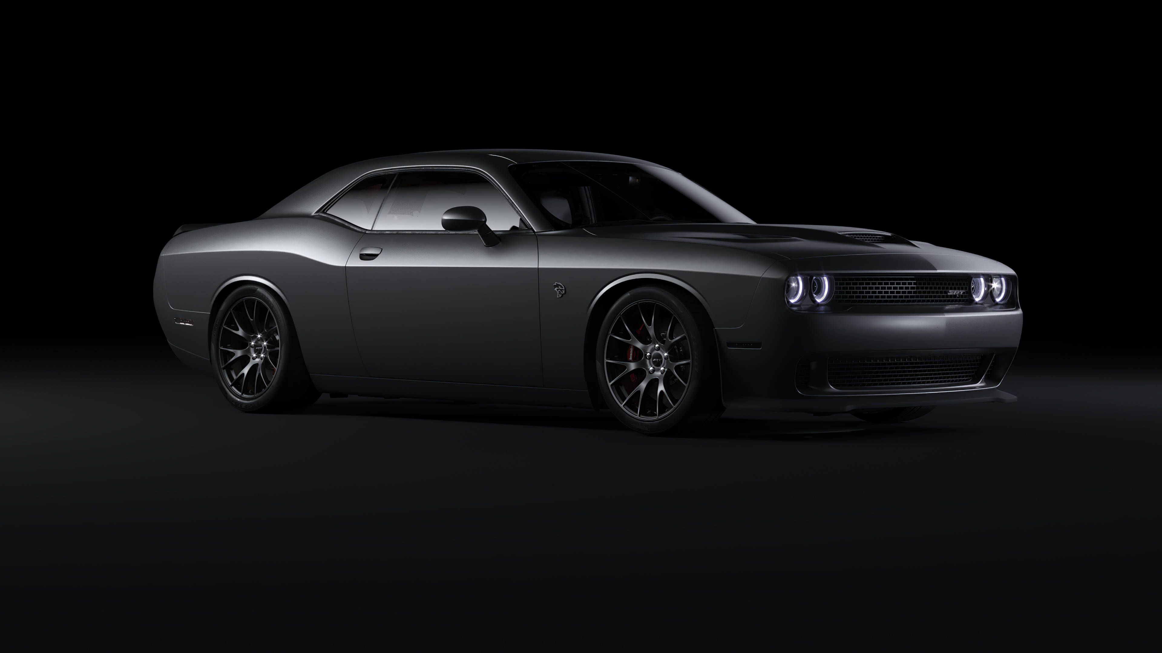 Dodge 桌布 壁紙 — 一輛時尚的啞光黑色道奇挑戰者跑車在純黑色工作室背景下閃爍著照亮的前燈。
