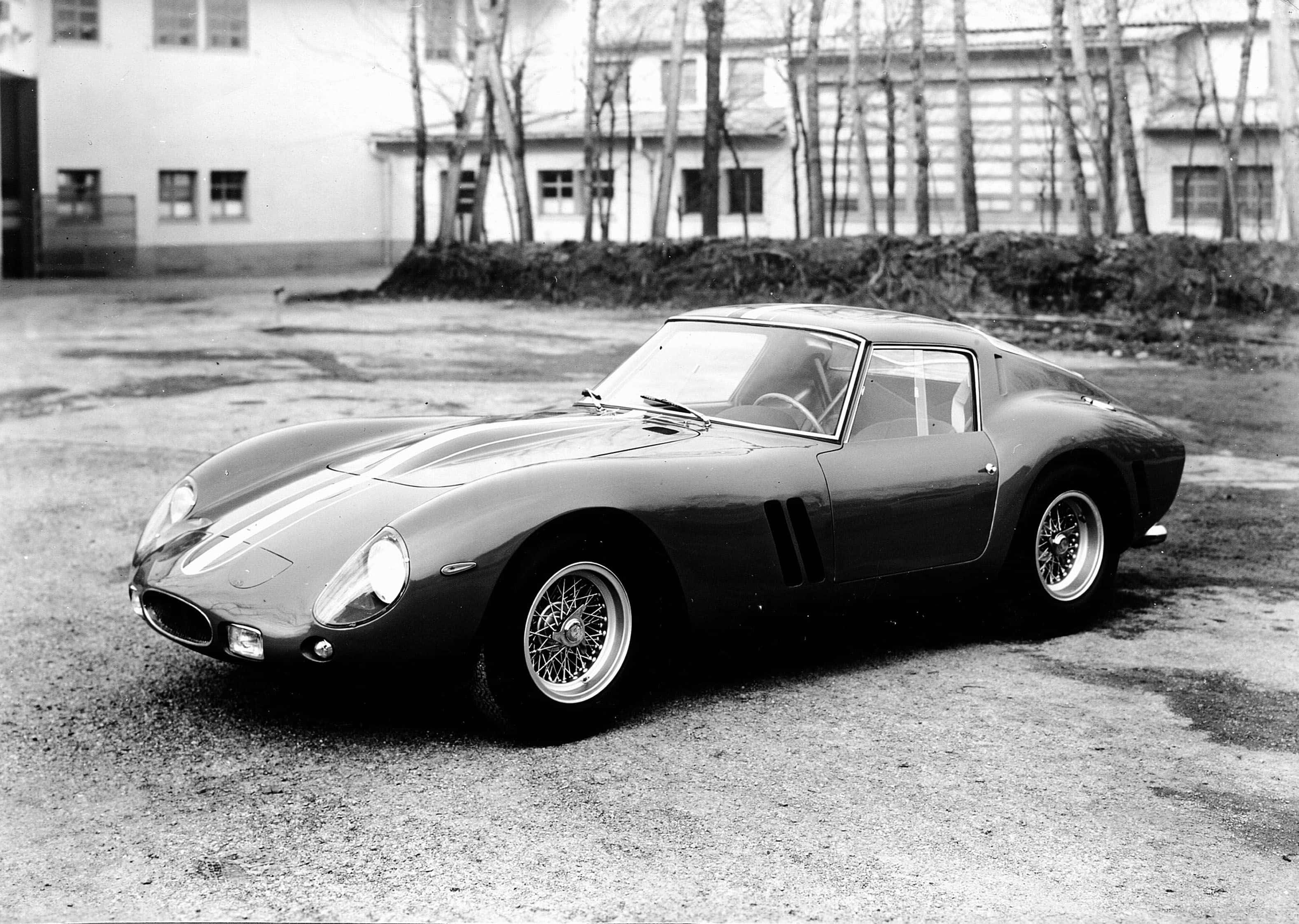 Black And White Vintage Car 桌布 壁紙 — 一輛時尚的復古法拉利250 GTO停放在建築物前的碎石地上，背景有光禿禿的樹木。