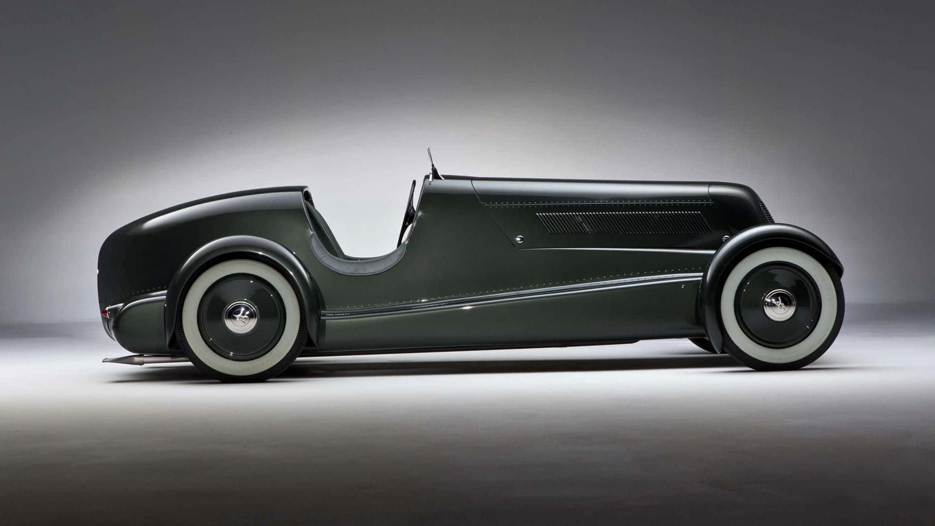 Car Design 桌布 壁紙 — 一輛時尚的復古賽車，採用消光深綠色車身和白色側壁輪胎，在極簡灰色工作室背景前蓄勢待發。