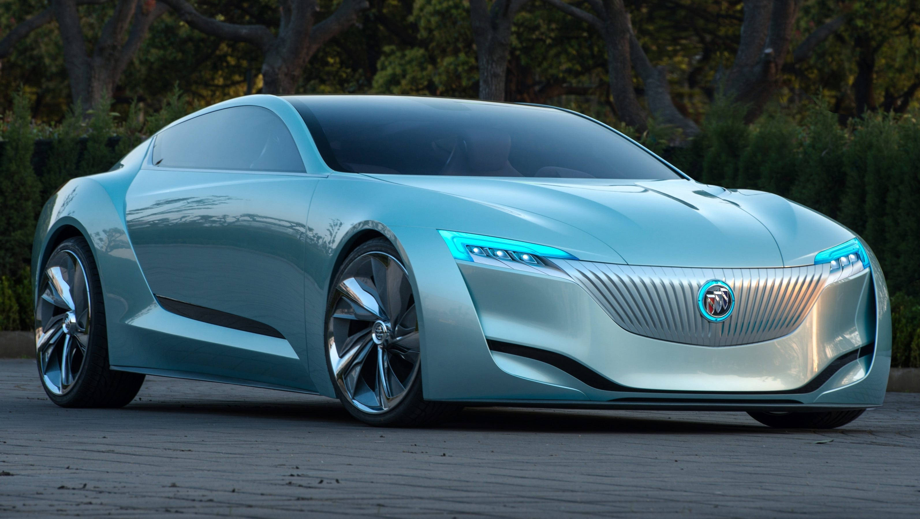 Buick 桌布 壁紙 — 一輛時尚的未來主義淺藍色概念車，帶有發光頭燈，停在鋪砌的小路上，周圍環繞著樹木。