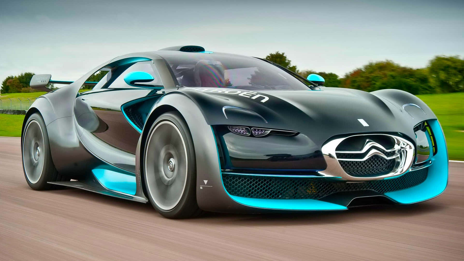 Citroen 桌布 壁紙 — 一輛時尚的未來主義跑車，帶有發光的藍色裝飾，沿著一條穿過綠色景觀的道路飛馳。