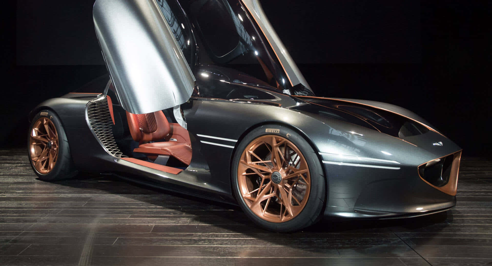 Genesis Essentia 桌布 壁紙 — 一輛時尚的未來主義跑車，配備鷗翼車門和銅色點綴，在深色木地板上於攝影棚燈光下閃閃發光。