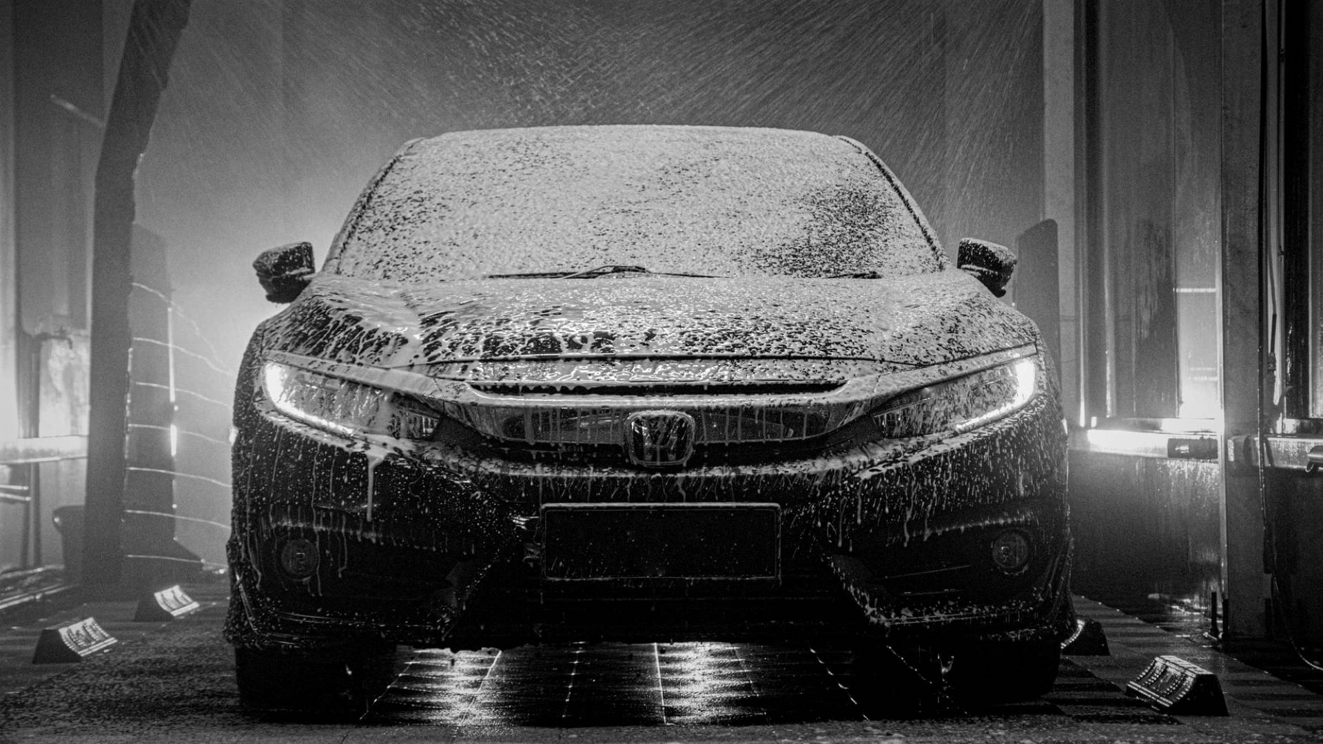 Wash 桌布 壁紙 — 一輛時尚的本田汽車在光線昏暗的洗車間內，被強力水柱沖洗，車身佈滿肥皂泡。