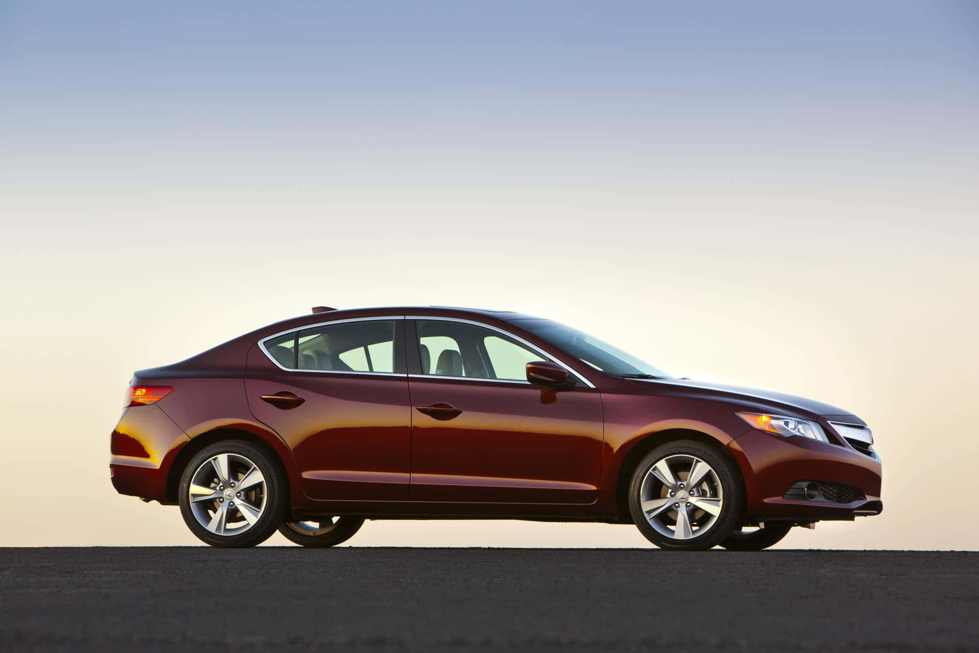Acura Ilx 桌布 壁紙 — 一輛時尚的栗色轎車在柔和的金色時光下閃耀，背景是漸變的天空。