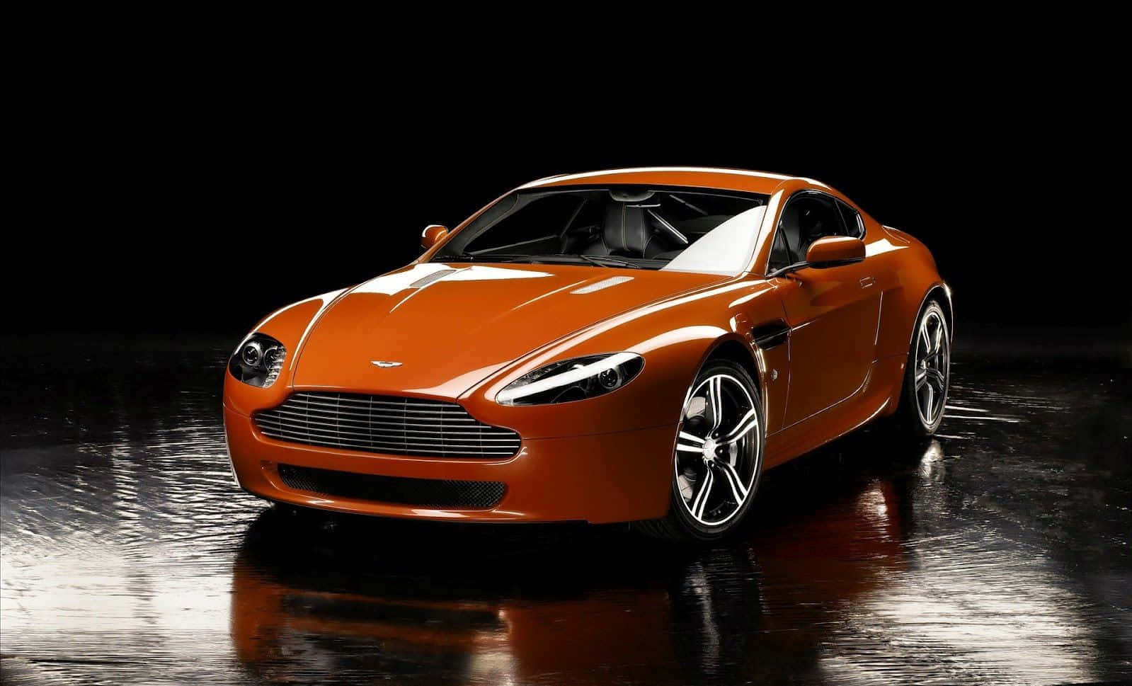 Top 10 Car 桌布 壁紙 — 一輛時尚的橙色Aston Martin跑車在黑色背景前的濕滑反光地板上，於攝影棚燈光下閃閃發光。