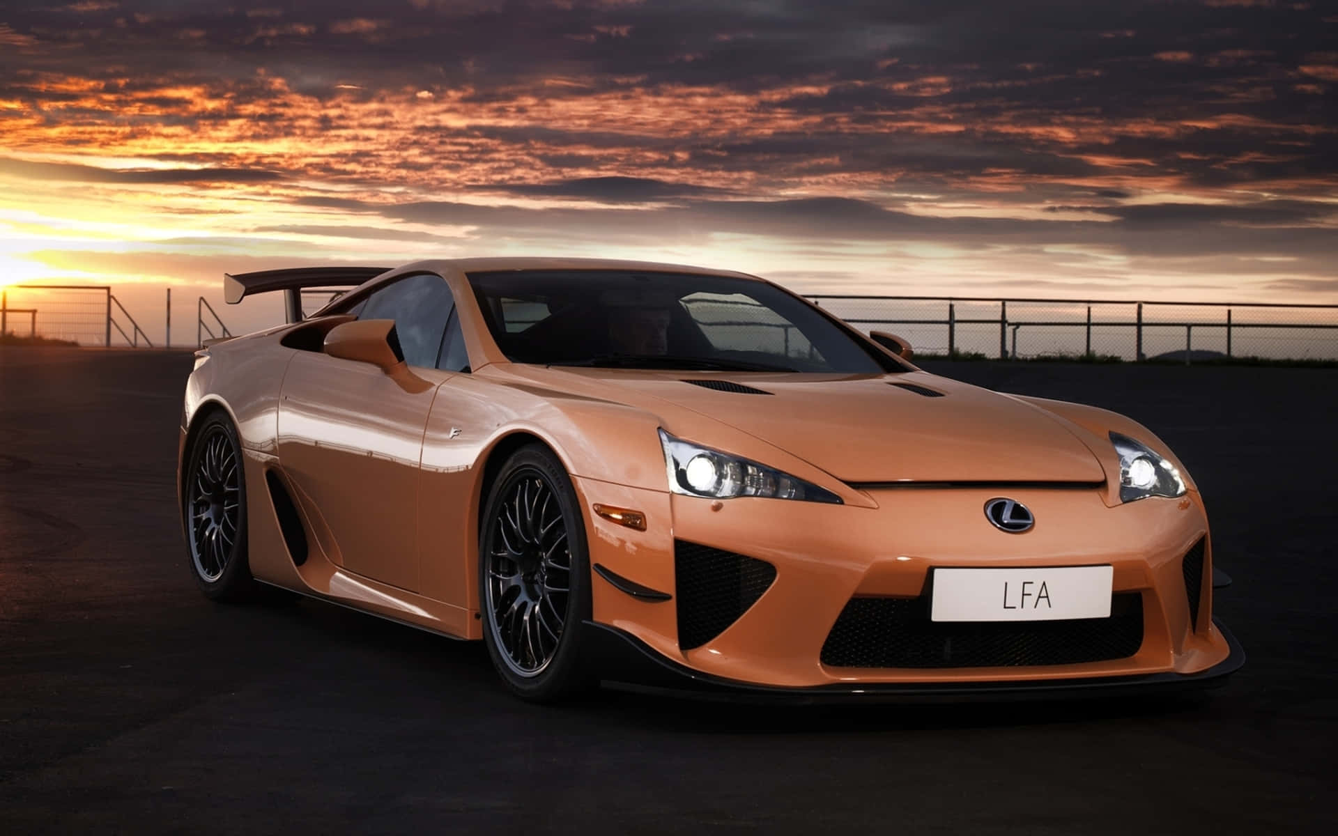 Lexus Lfa 桌布 壁紙 — 一輛時尚的橙色Lexus LFA跑車在戲劇性雲層的熾熱日落天空下閃耀。