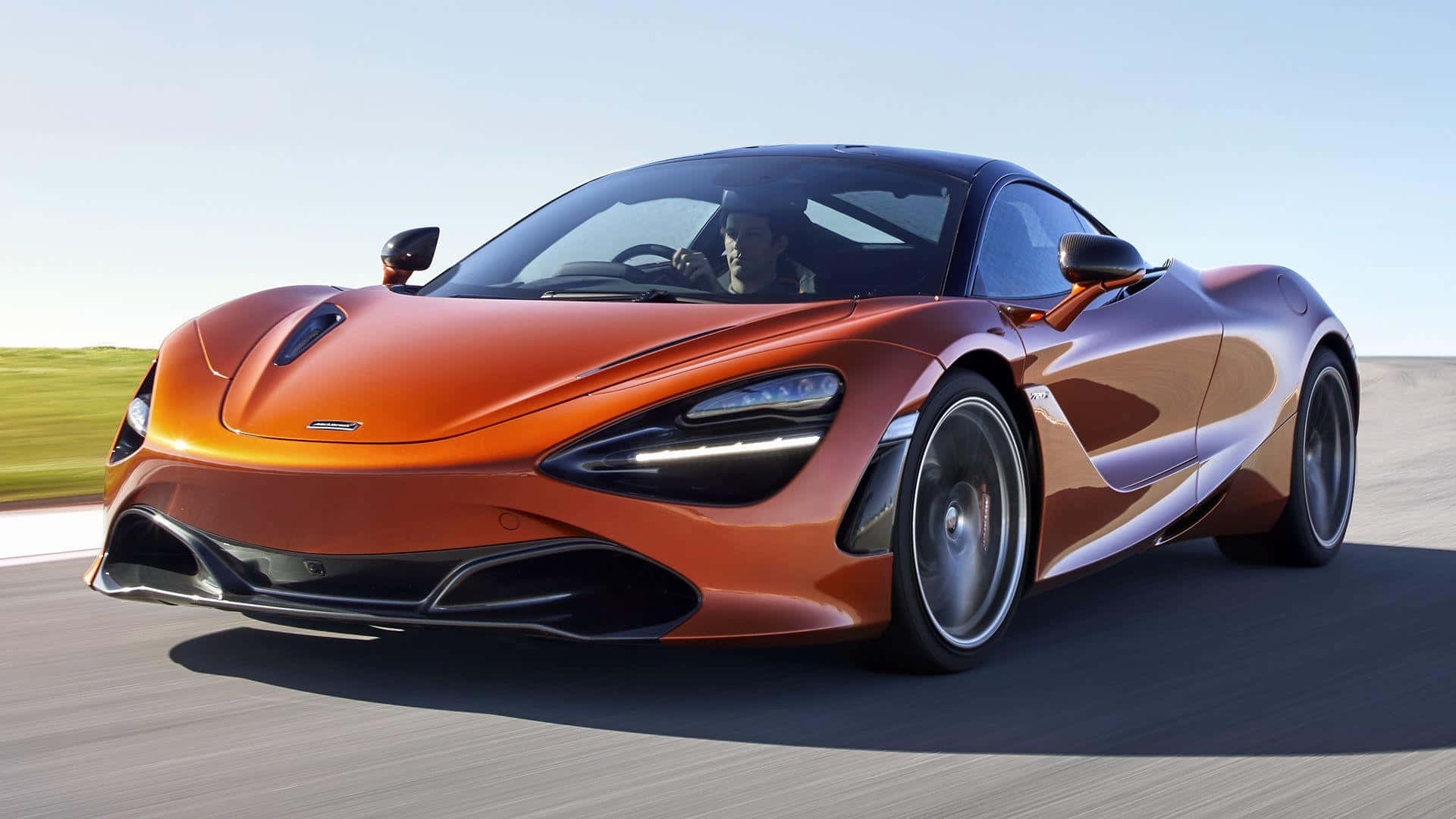 麥拉倫 720S 桌布 壁紙 — 一輛時尚的橙色McLaren 720S跑車在陽光明媚的賽道上疾馳，背景是模糊的綠色田野。