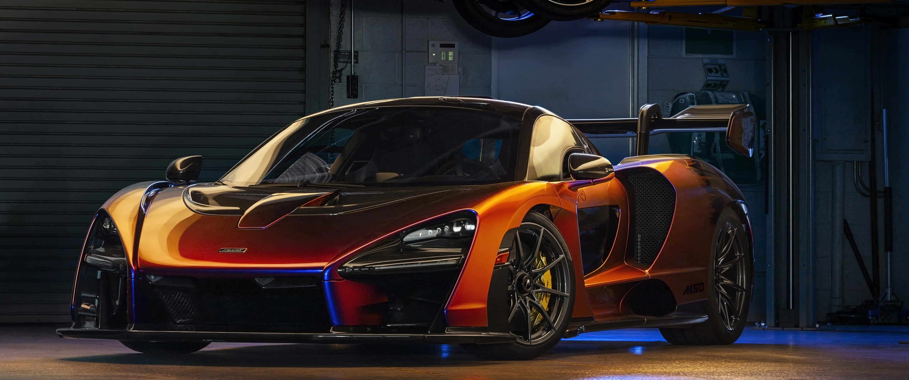 Cool Mclaren 桌布 壁紙 — 一輛時尚的橙色McLaren Senna跑車在昏暗的車庫中，在藍色燈光下閃閃發光。