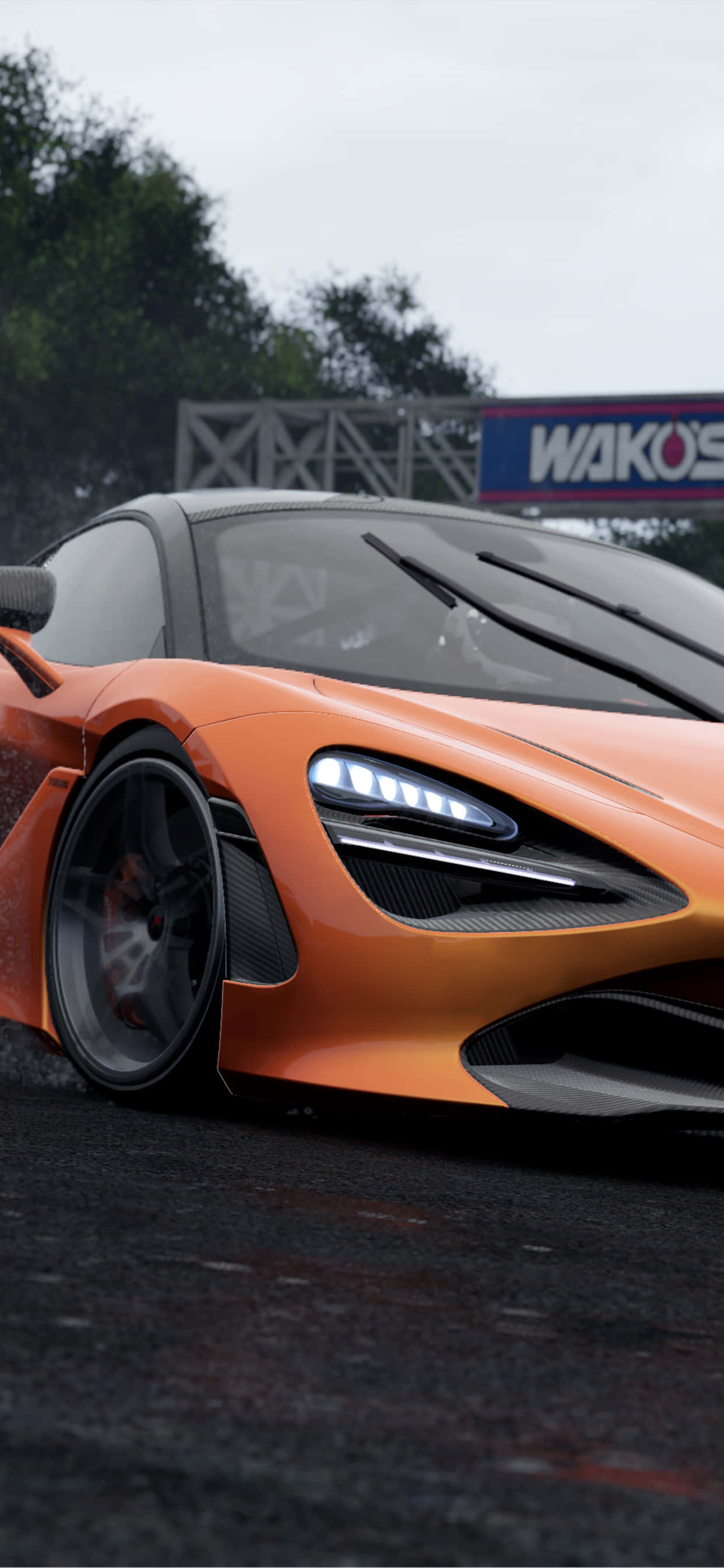 電玩遊戲 桌布 壁紙 — 一輛時尚的橙色McLaren跑車，車頭燈發光，停泊在潮濕的賽道上，天空多雲。
