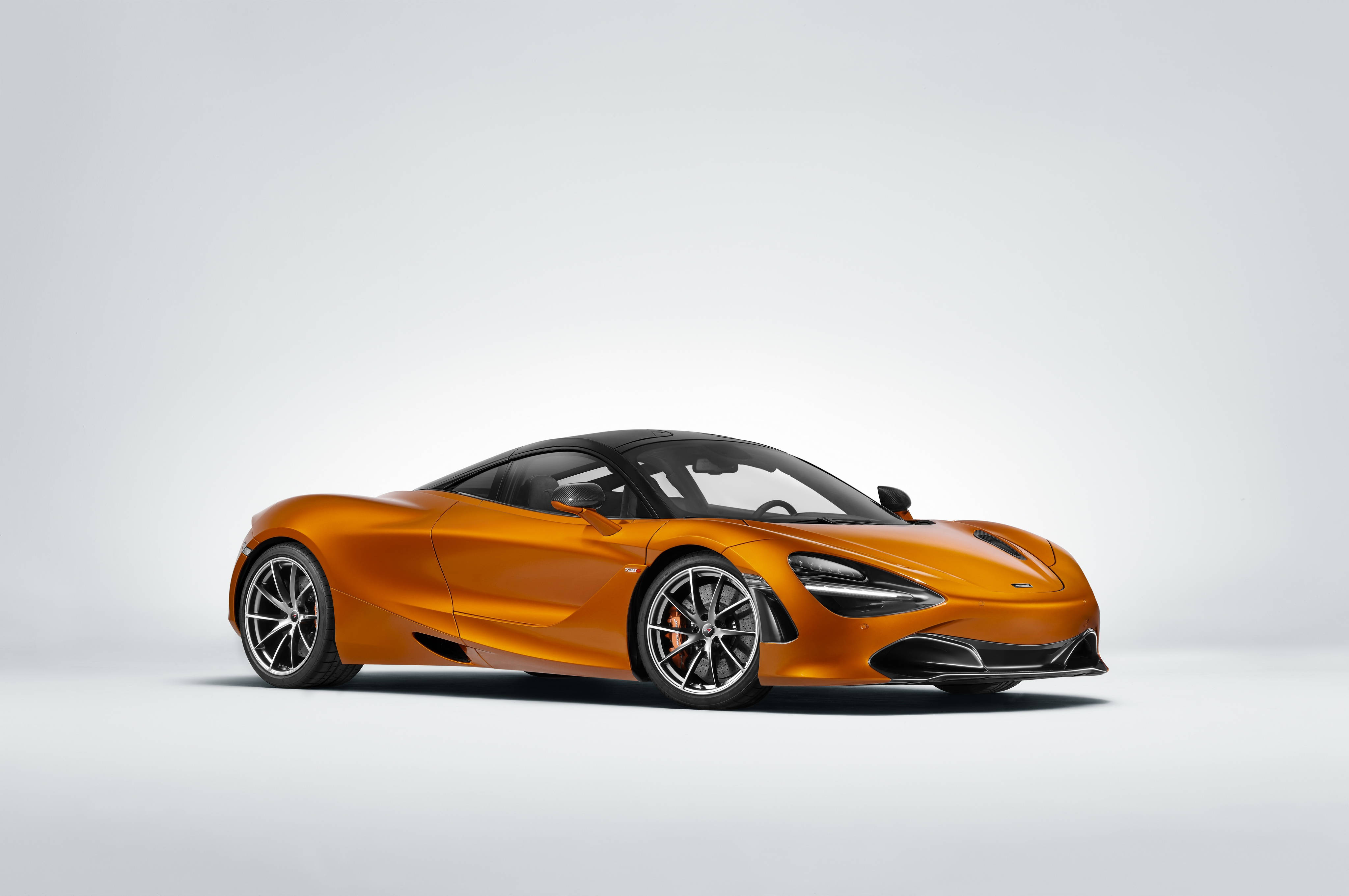 mclaren 720s 4K 桌布 壁紙 — 一輛時尚的橙色McLaren跑車，帶有黑色飾邊和銀色輪圈，擺放在極簡的白色工作室背景前。