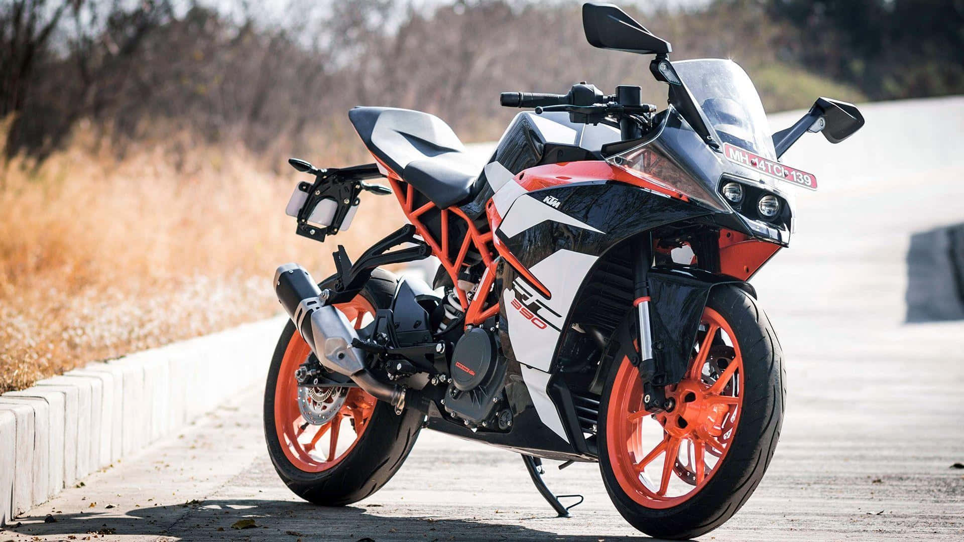 HD Bikes 桌布 壁紙 — 一輛時尚的橙色和黑色KTM機車停在路邊，背景有乾草和樹木。
