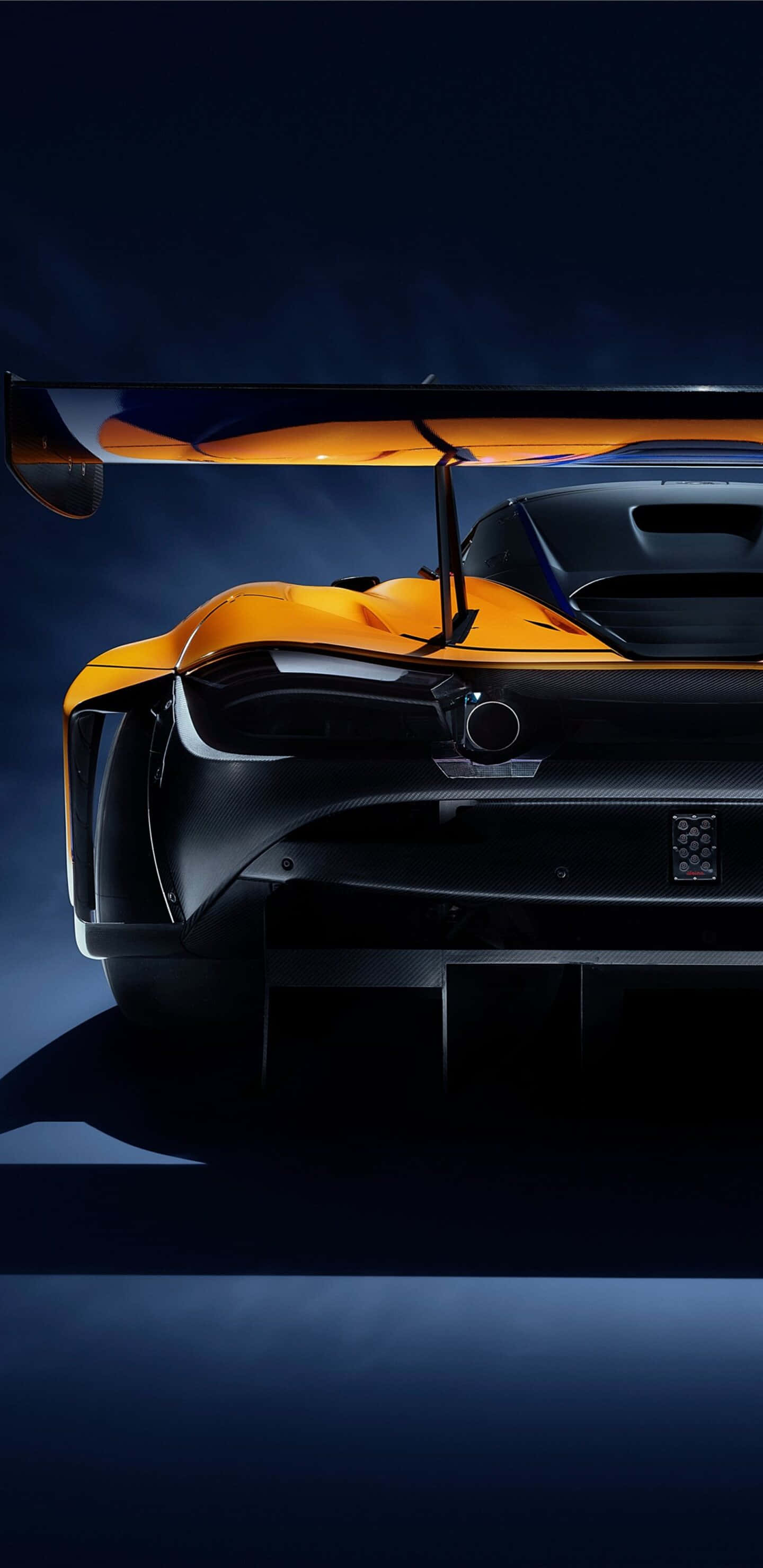 Pixel 3xl Mclaren 720s 桌布 壁紙 — 一輛時尚的橙色和黑色超跑，帶有巨大的後翼，在深藍色工作室背景下戲劇性地照亮。