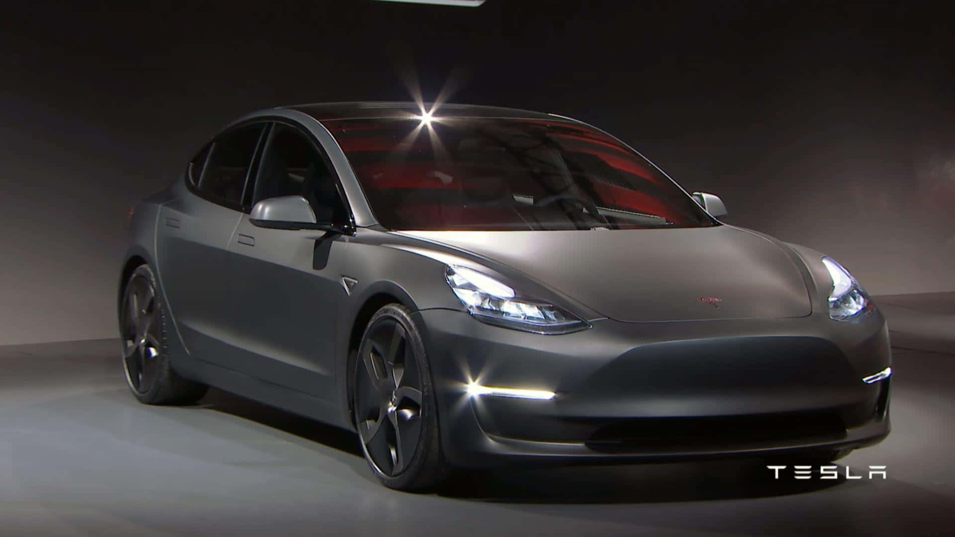 Tesla Model 3 桌布 壁紙 — 一輛時尚的消光灰色Tesla Model 3轎車在攝影棚燈光下閃耀，車頭燈發光，透過擋風玻璃可見紅色內裝。