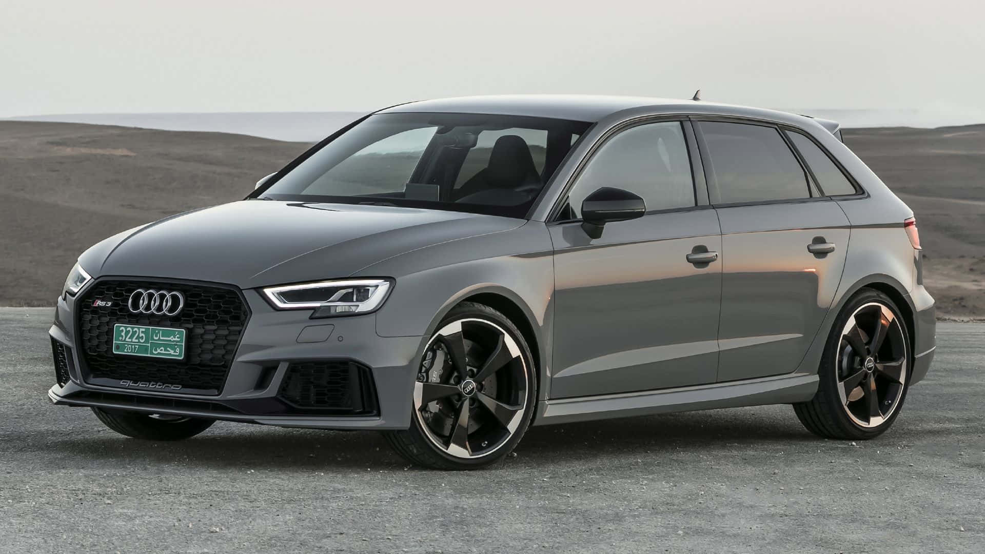 Audi Rs3 桌布 壁紙 — 一輛時尚的消光灰色奧迪RS3 Sportback停在碎石路面上，背景是荒蕪的沙漠景觀和遠處的地平線，光線柔和。