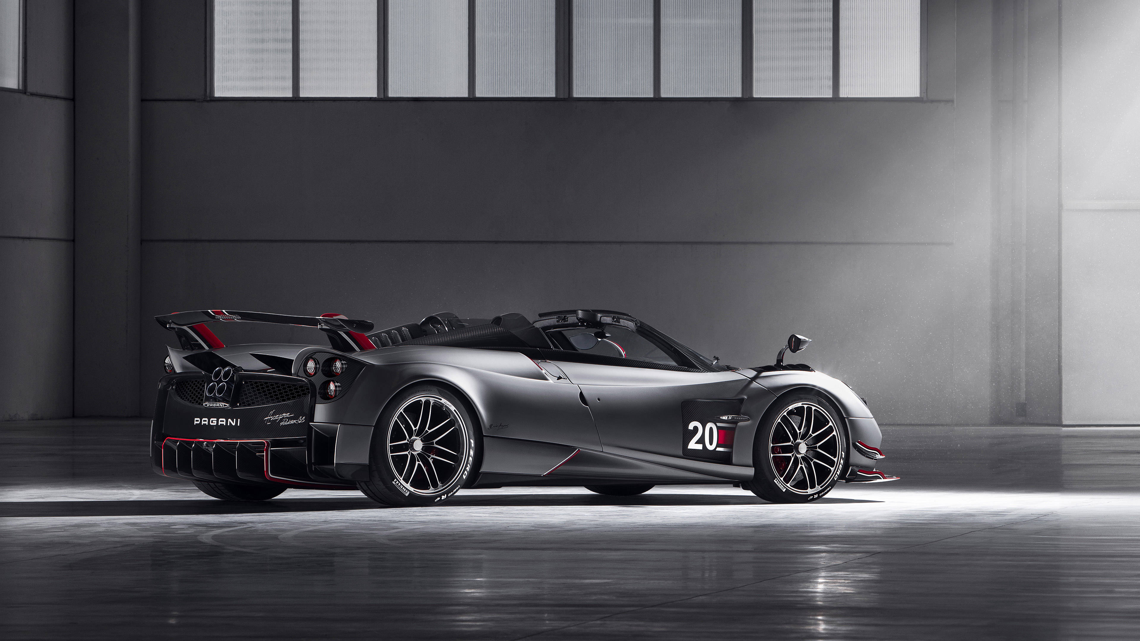 pagani iPhone 桌布 壁紙 — 一輛時尚的消光灰色帕加尼Zonda賽車，帶有紅色點綴和20號車牌，停在簡約工業倉庫中，燈光效果戲劇化。
