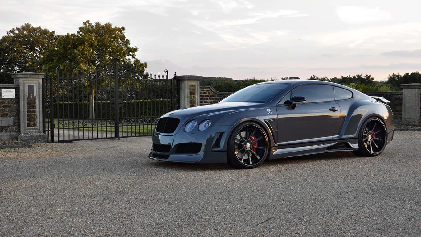 1366x768 Bentley 桌布 壁紙 — 一輛時尚的消光灰色賓利 Continental GT 在黃昏時分疾速駛過有閘門的莊園車道。